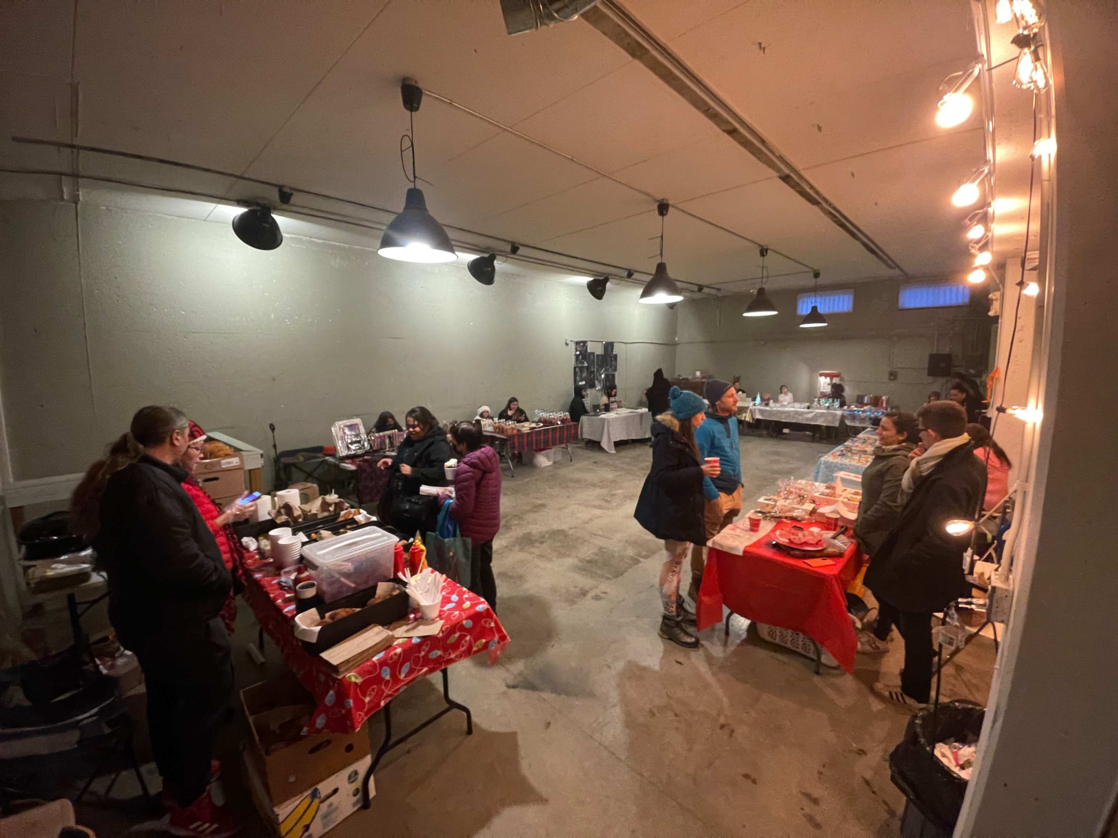 A spacious indoor market scene shows various vendors and customers engaged in activities at tables adorned with red tablecloths.