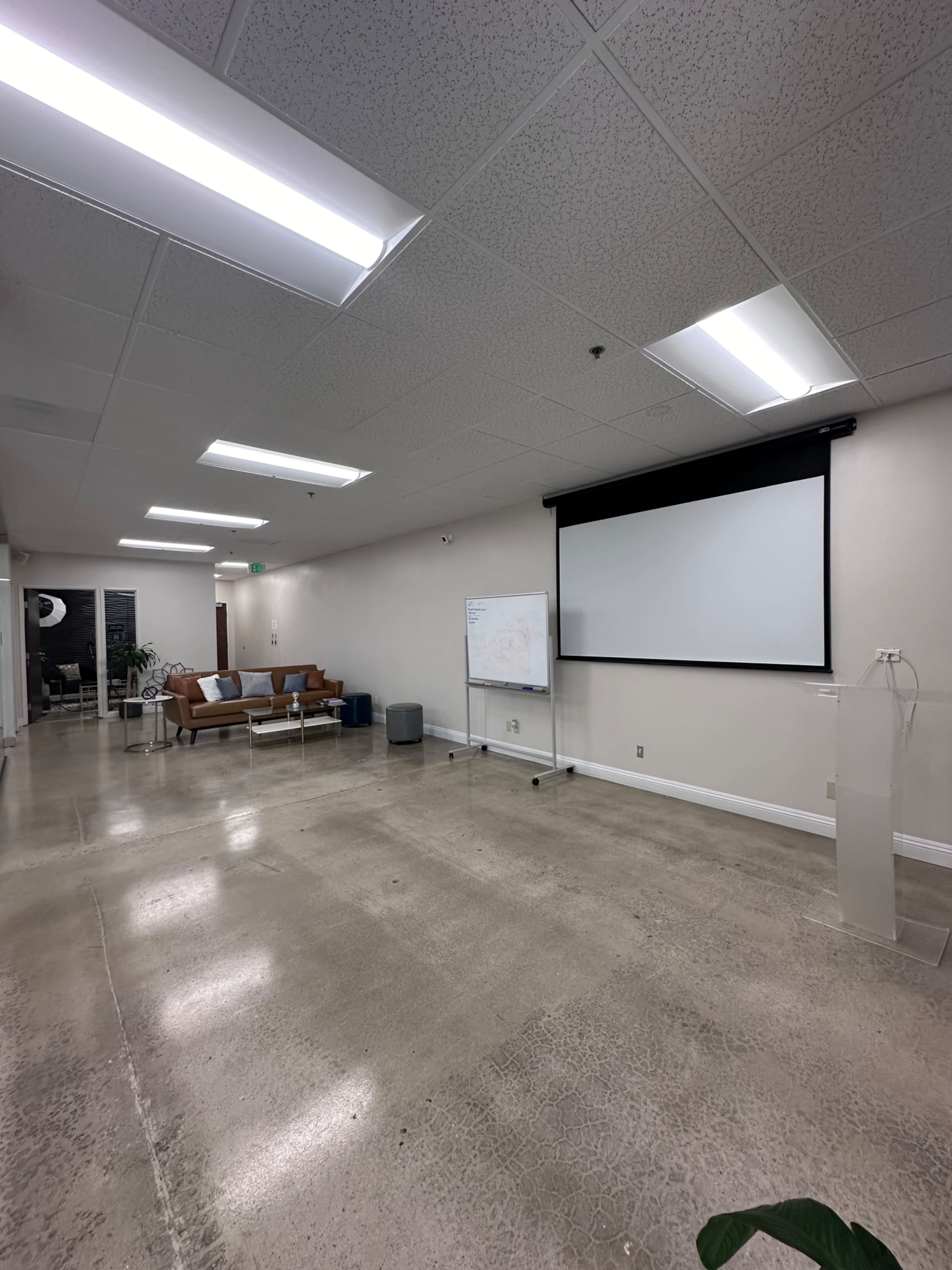 A spacious meeting room with a seating area, a whiteboard, and a large screen against the wall.