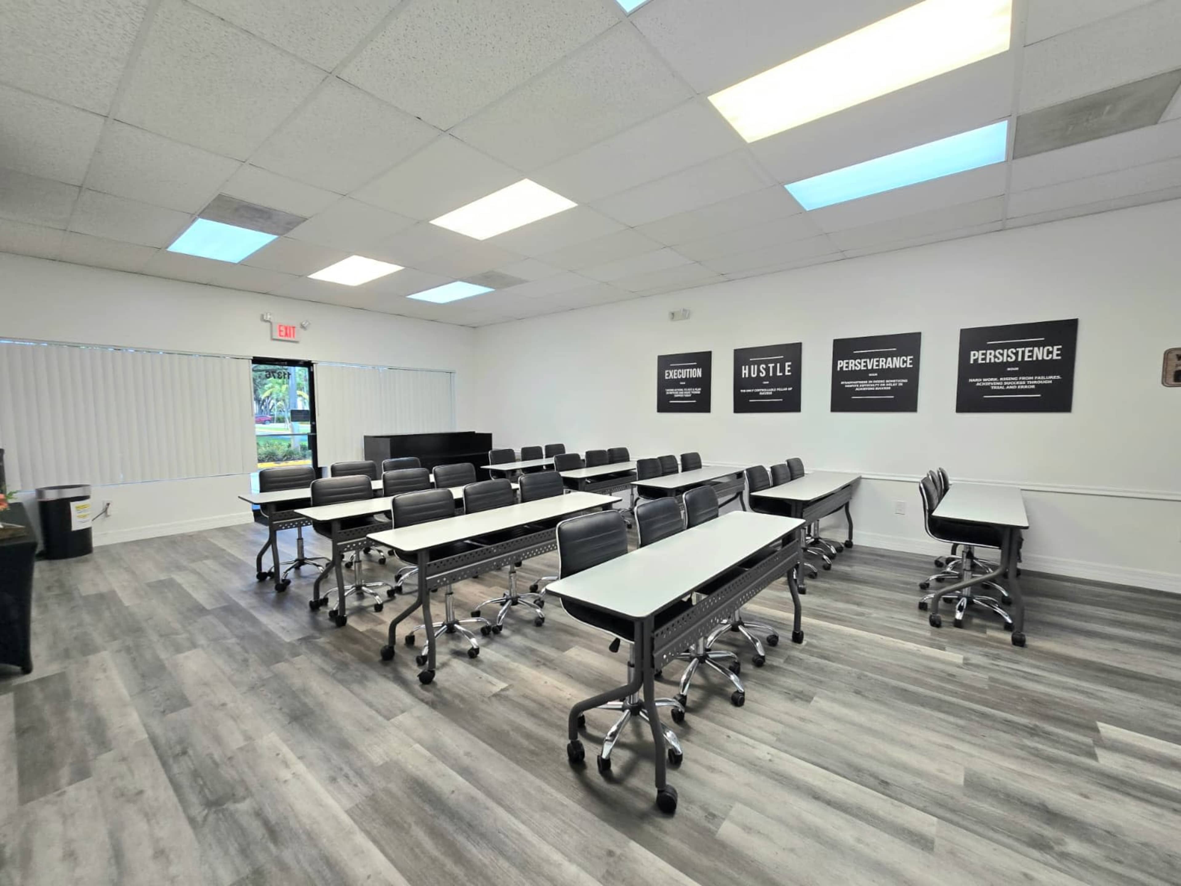 The image shows a classroom setup with rows of tables and chairs, along with motivational posters on the walls.