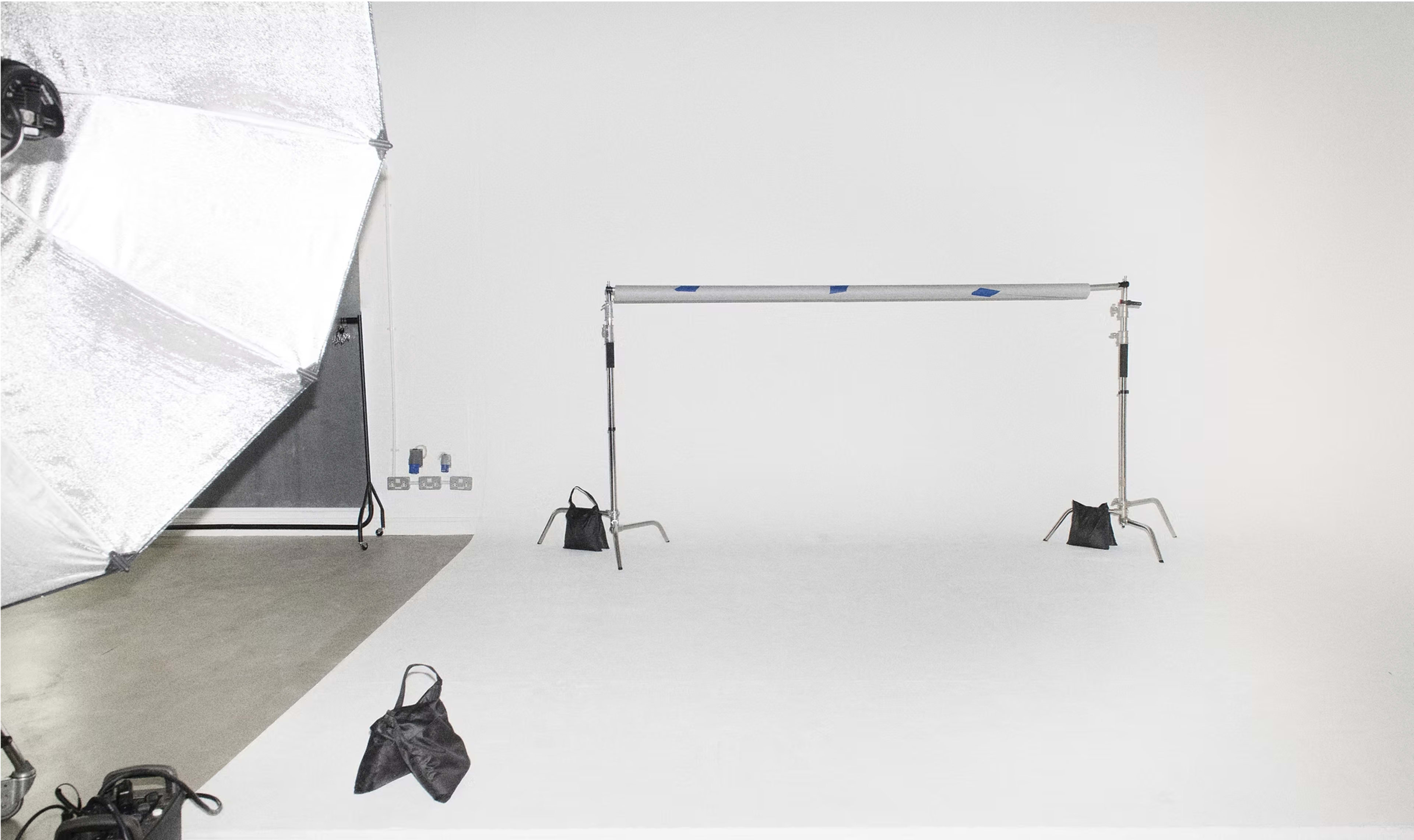 The image shows a photography studio setup with a softbox light and a backdrop support frame on a white floor.