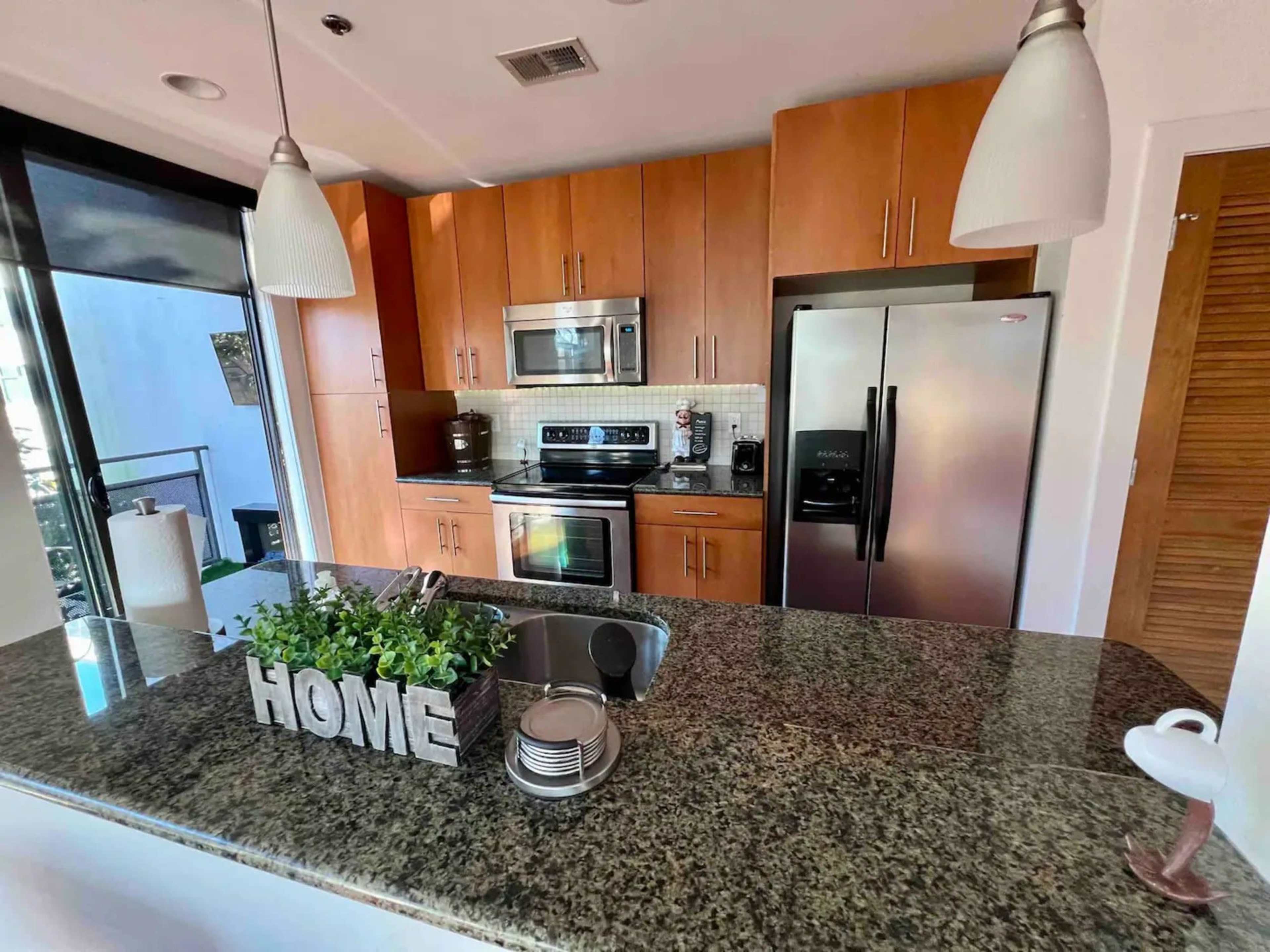 A modern kitchen with wooden cabinetry, stainless steel appliances, and a granite countertop featuring decorative items.