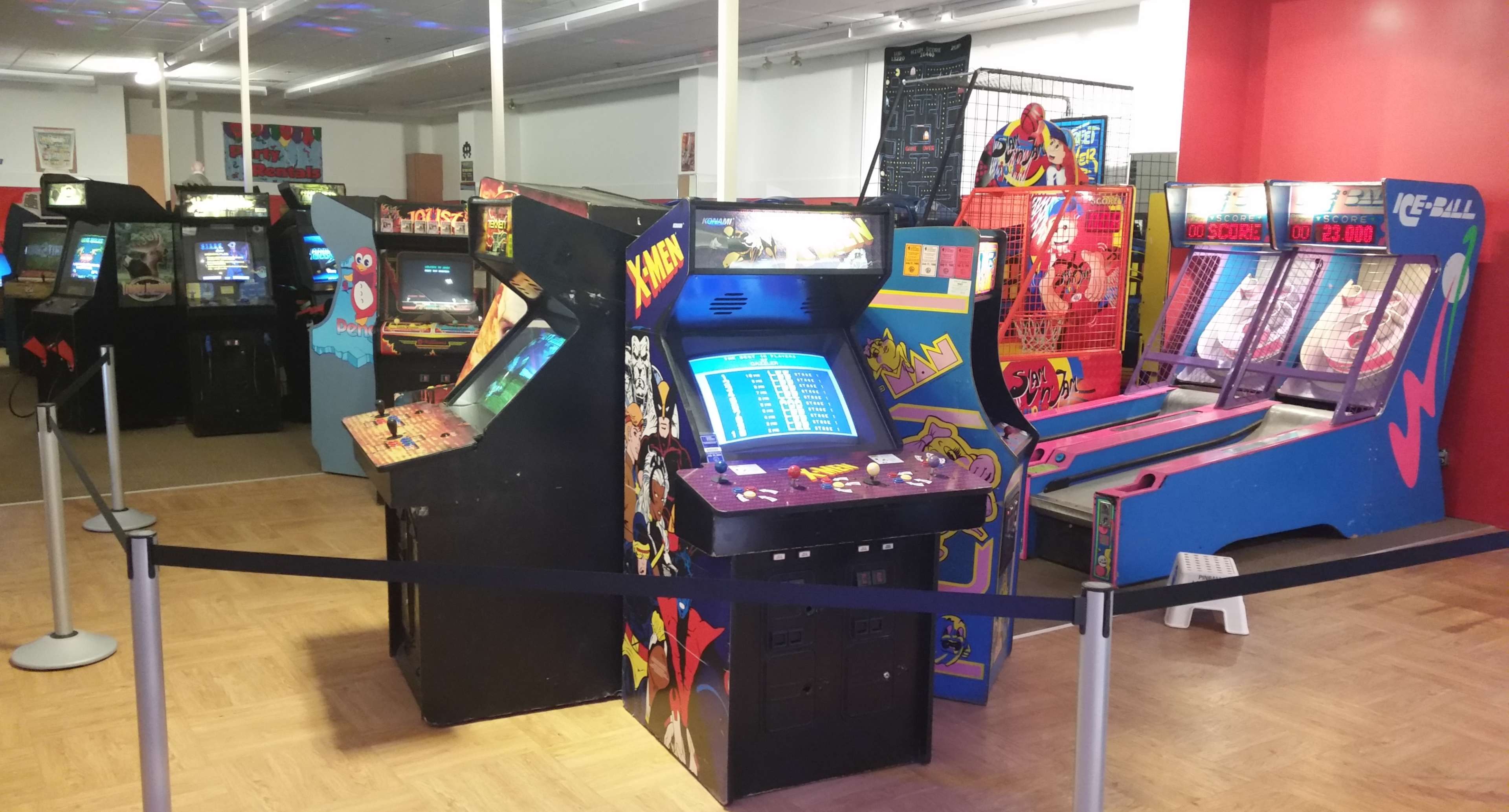 The image shows a row of classic arcade game machines in a brightly lit indoor arcade area.