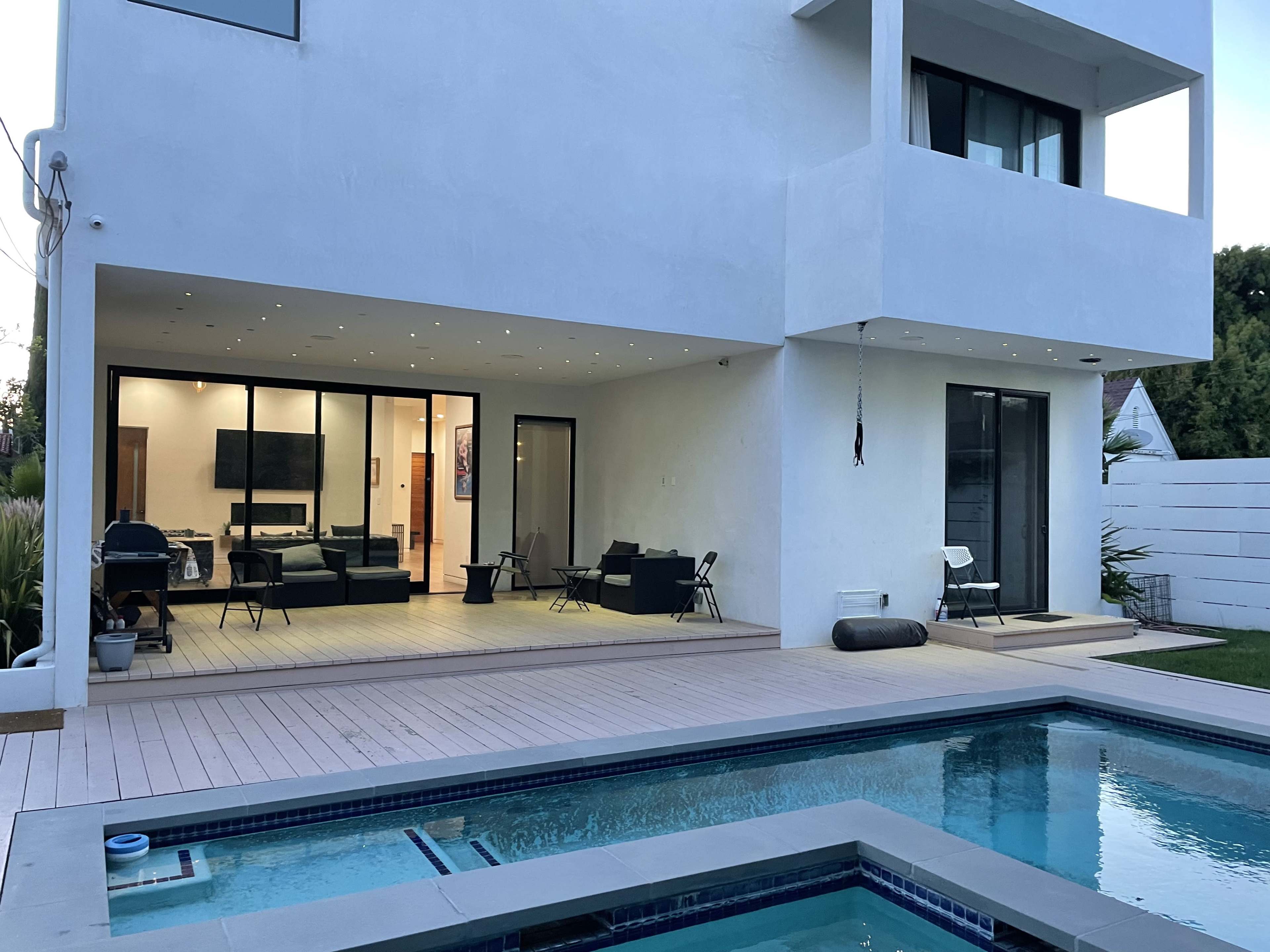 A modern two-story house with large glass doors, a well-lit interior, and a swimming pool in the foreground.