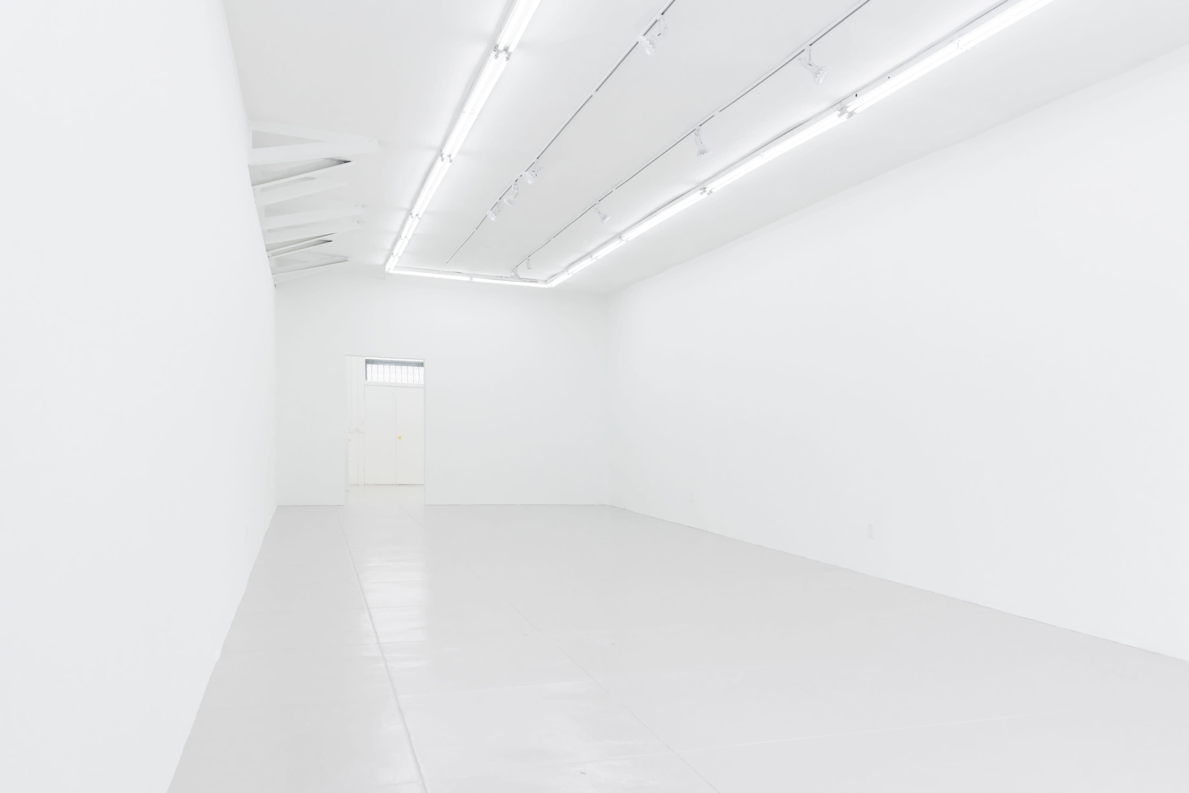 A minimalistic white room with a smooth floor, bright lighting, and a single door at the far end.