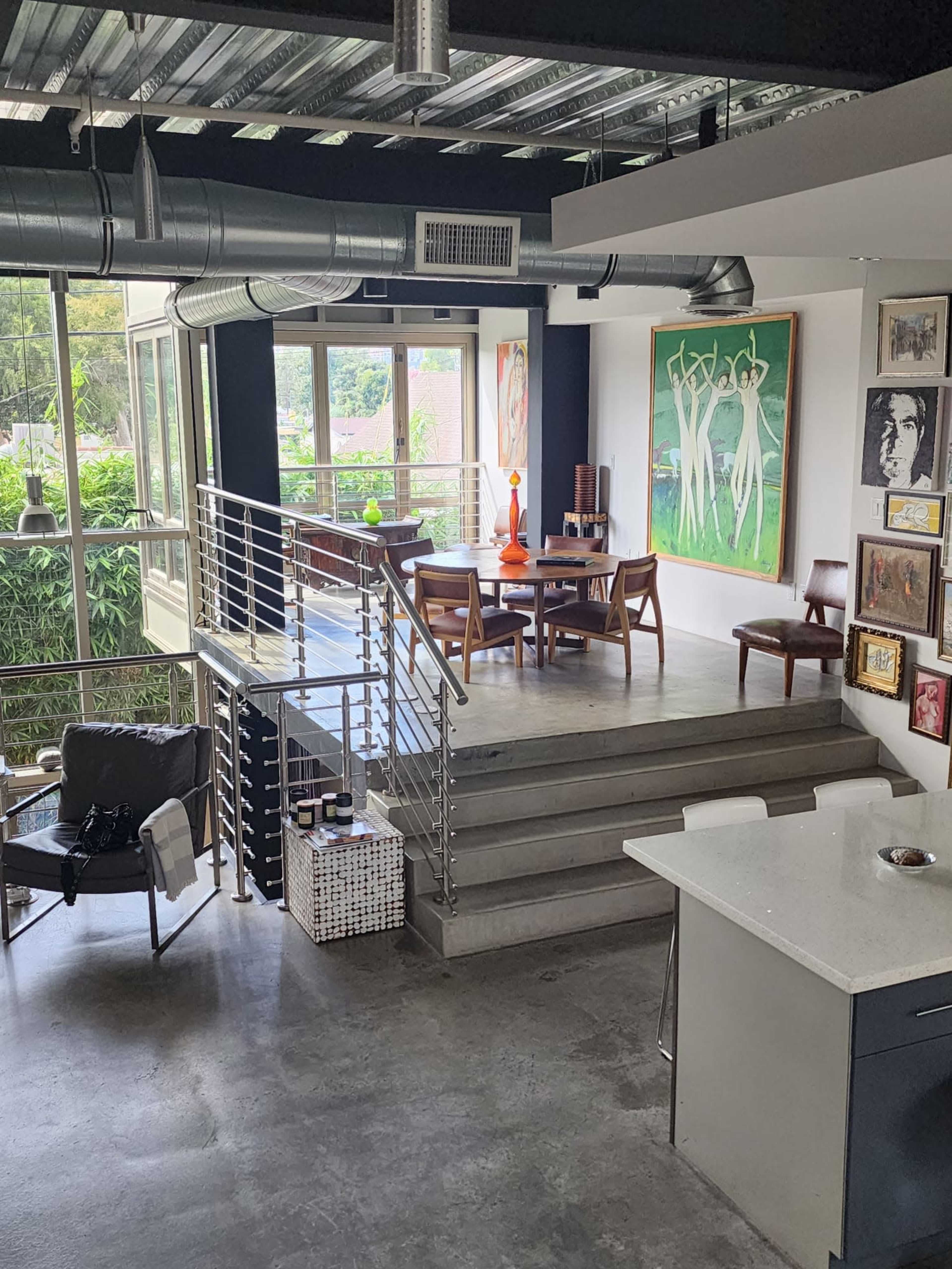A modern, open-concept living space with a dining area, artwork on the walls, and a staircase leading to the upper level.