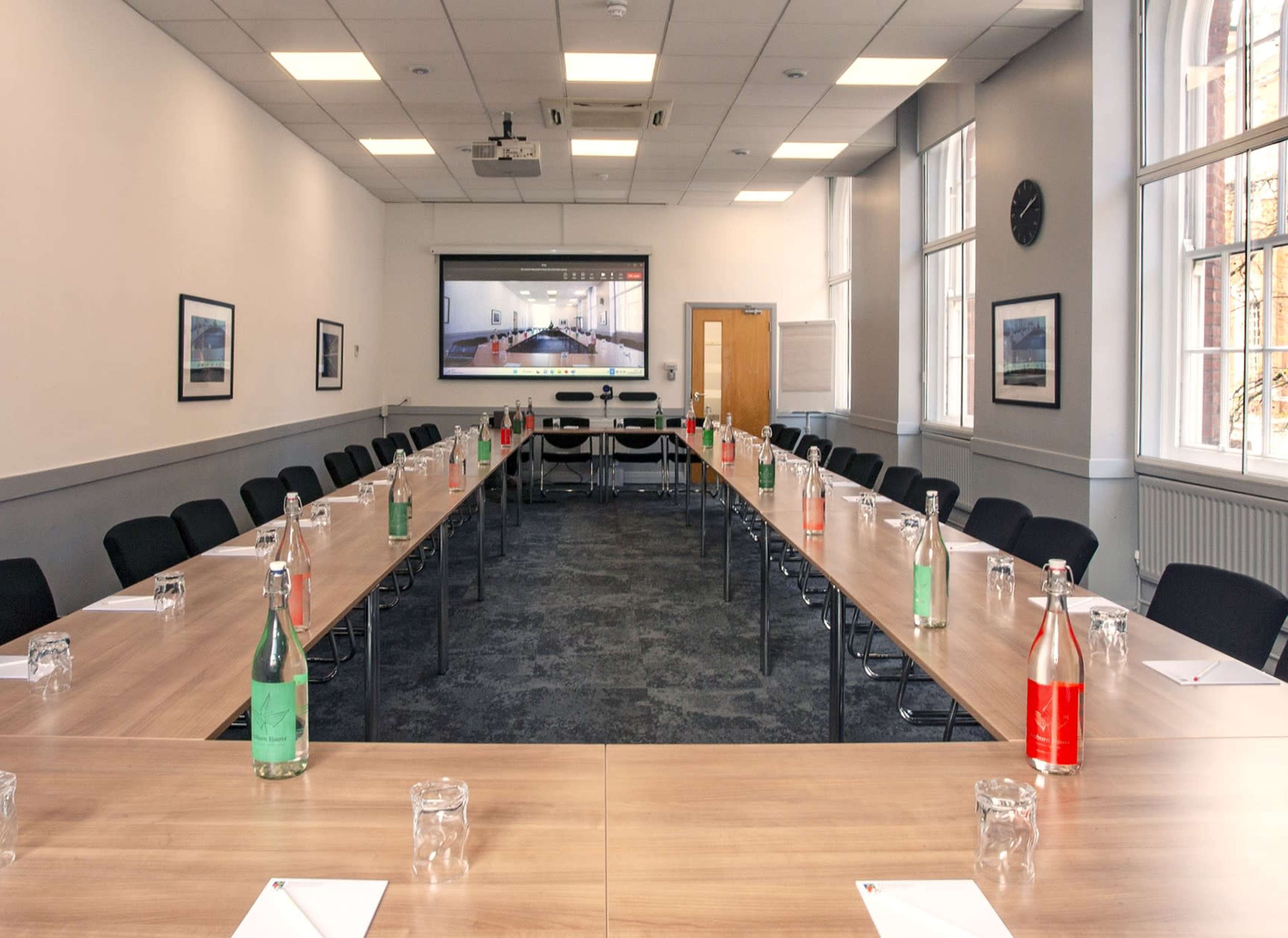 A conference room is arranged with a long table, chairs on either side, and bottles of water in various colors on the table.