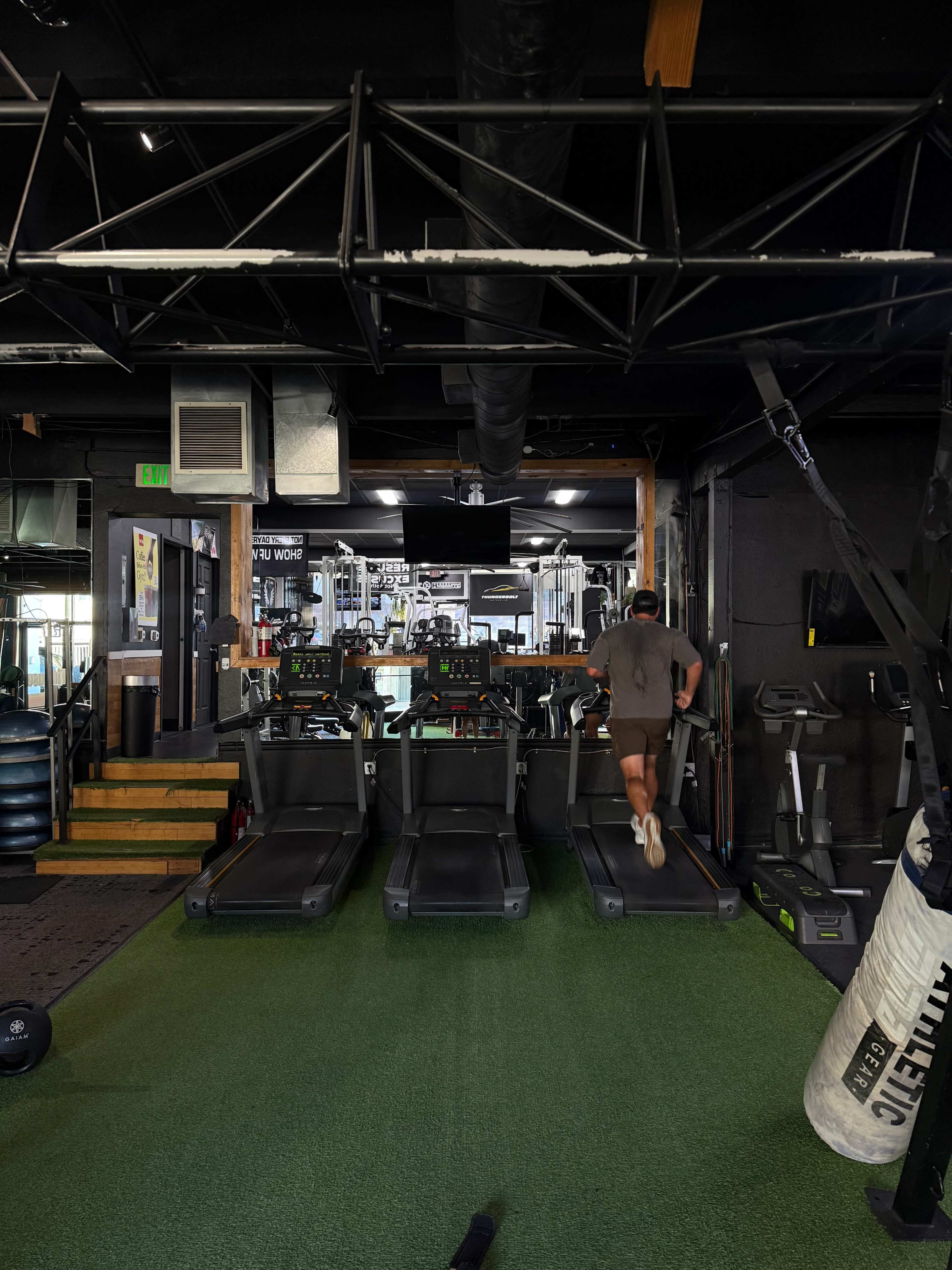 A person runs on a treadmill in a gym environment with exercise equipment visible in the background.