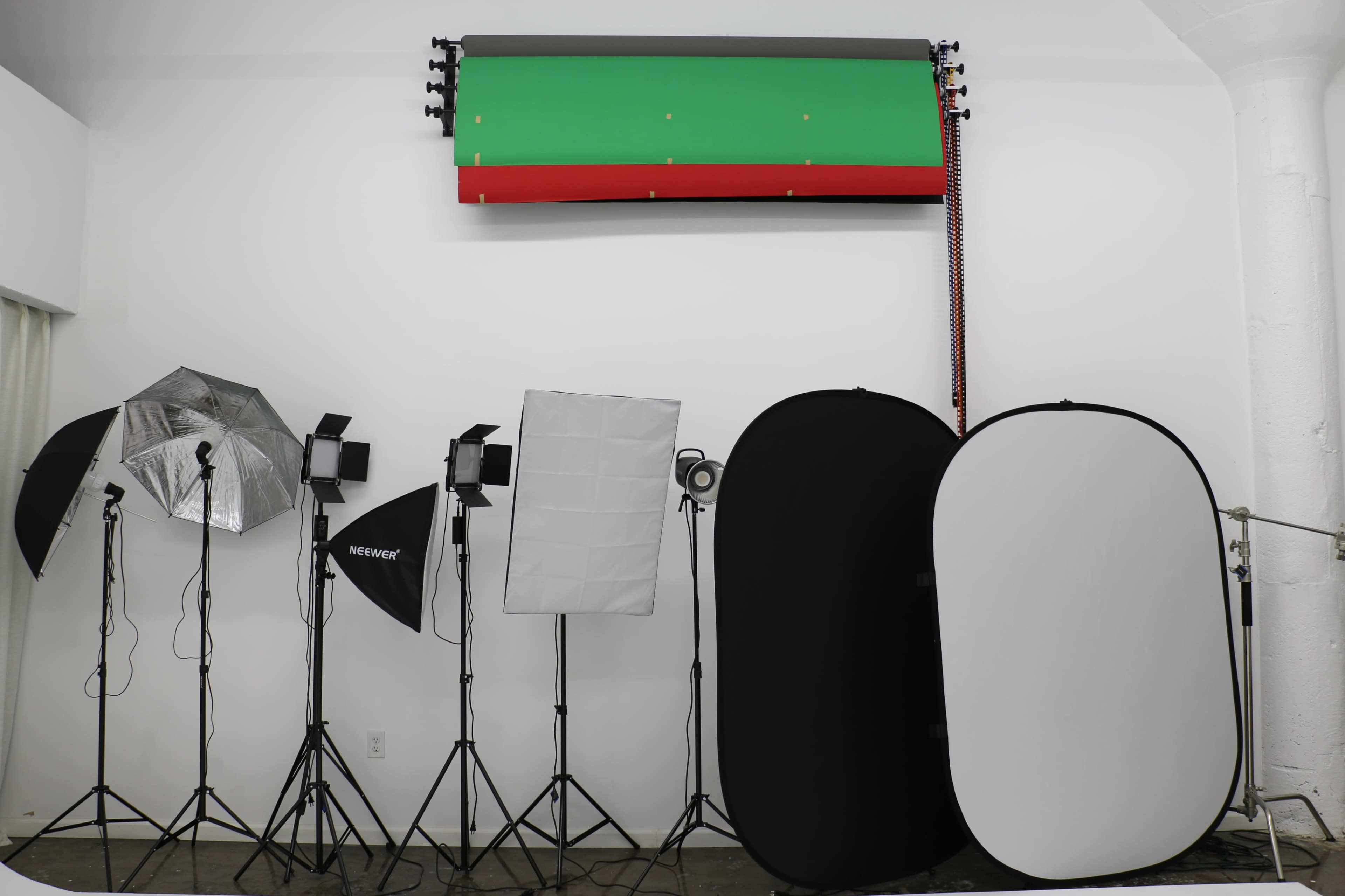 The image shows a photography studio setup with various lighting equipment, including softboxes and backdrops in green and red, along with reflective screens.