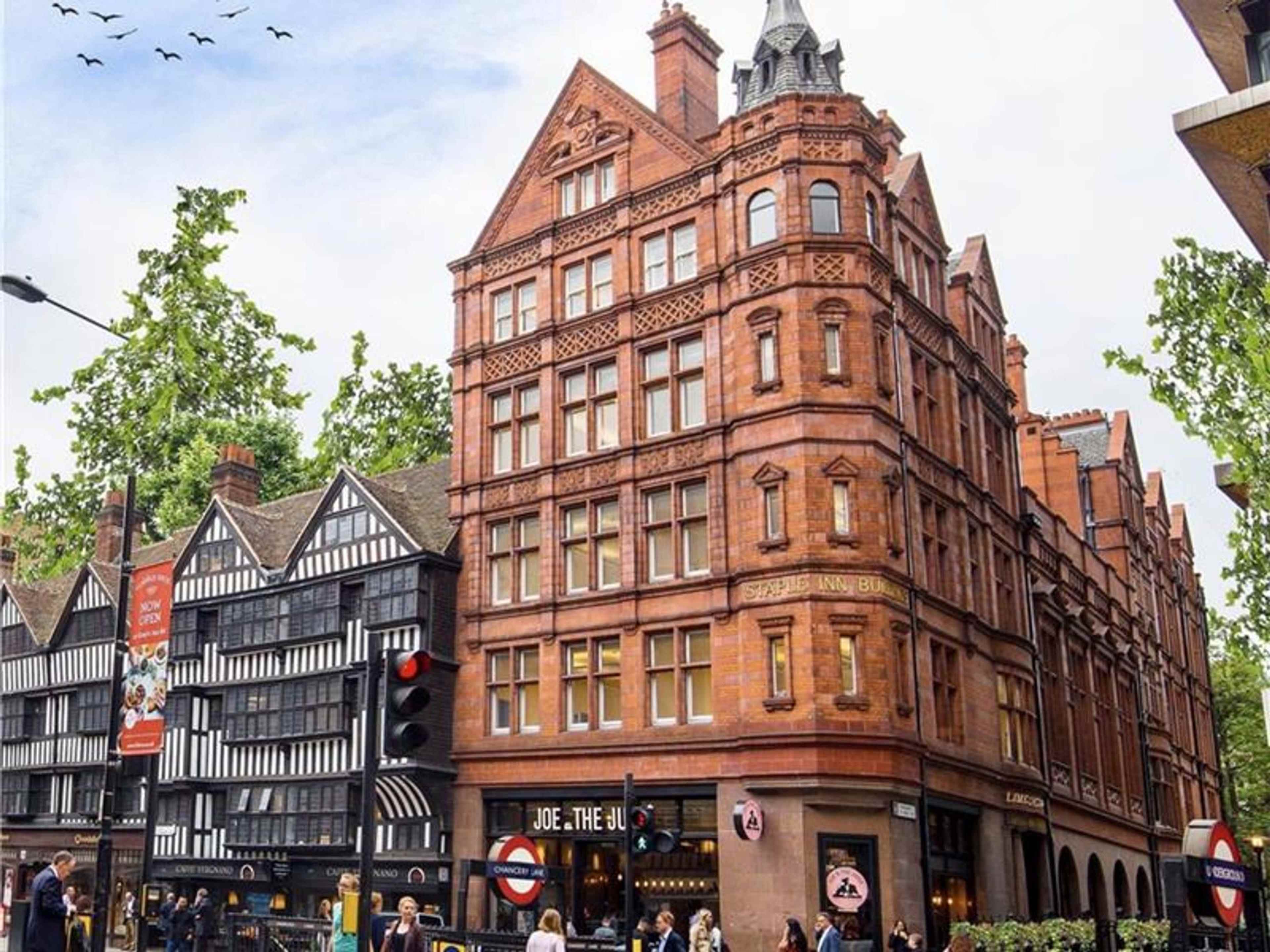 A street scene featuring a red-brick building with intricate architectural details next to a traditional black-and-white timber-framed structure.