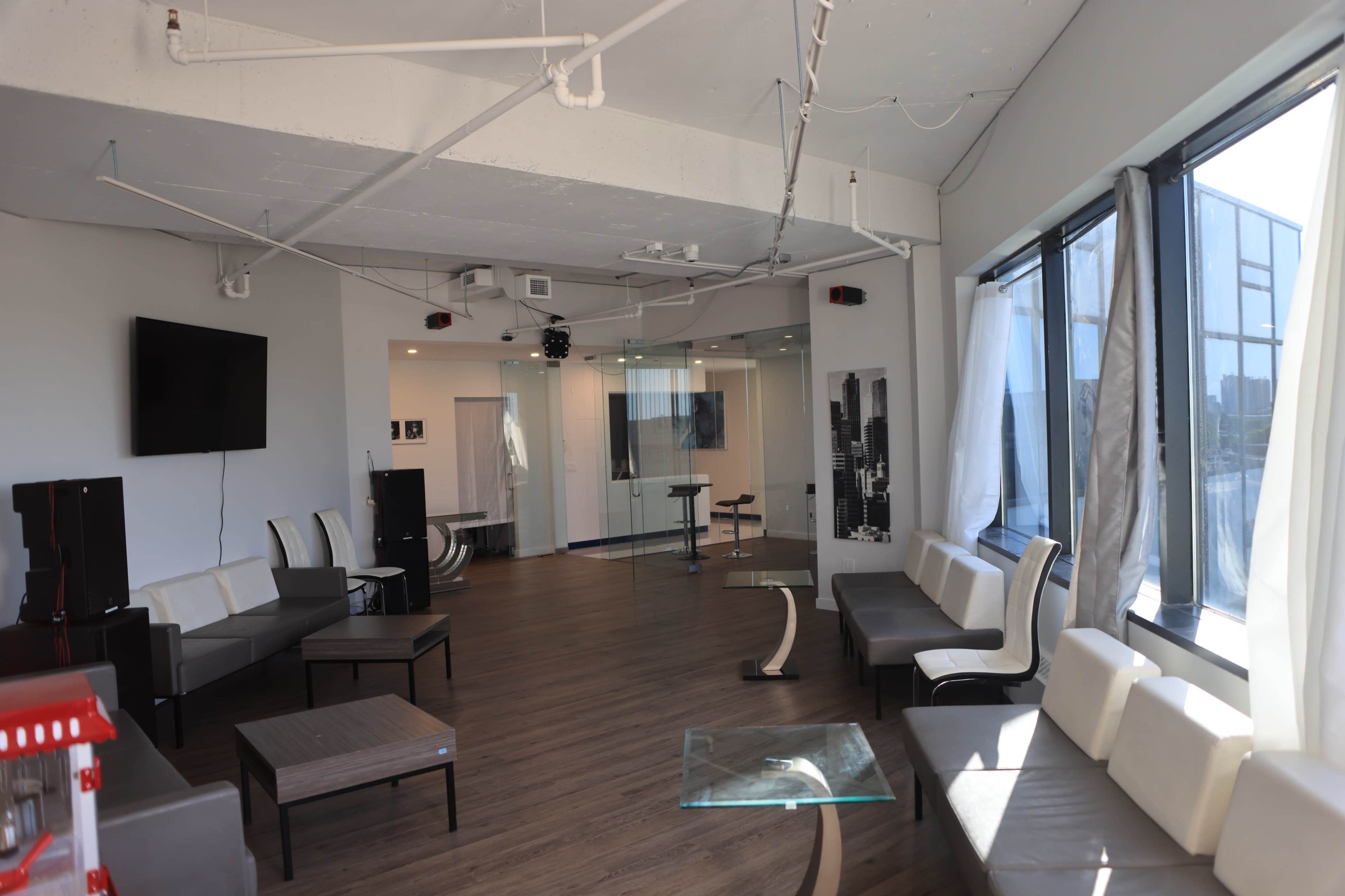 The image shows a modern, open lounge area with several couches, glass tables, and large windows allowing natural light to enter.