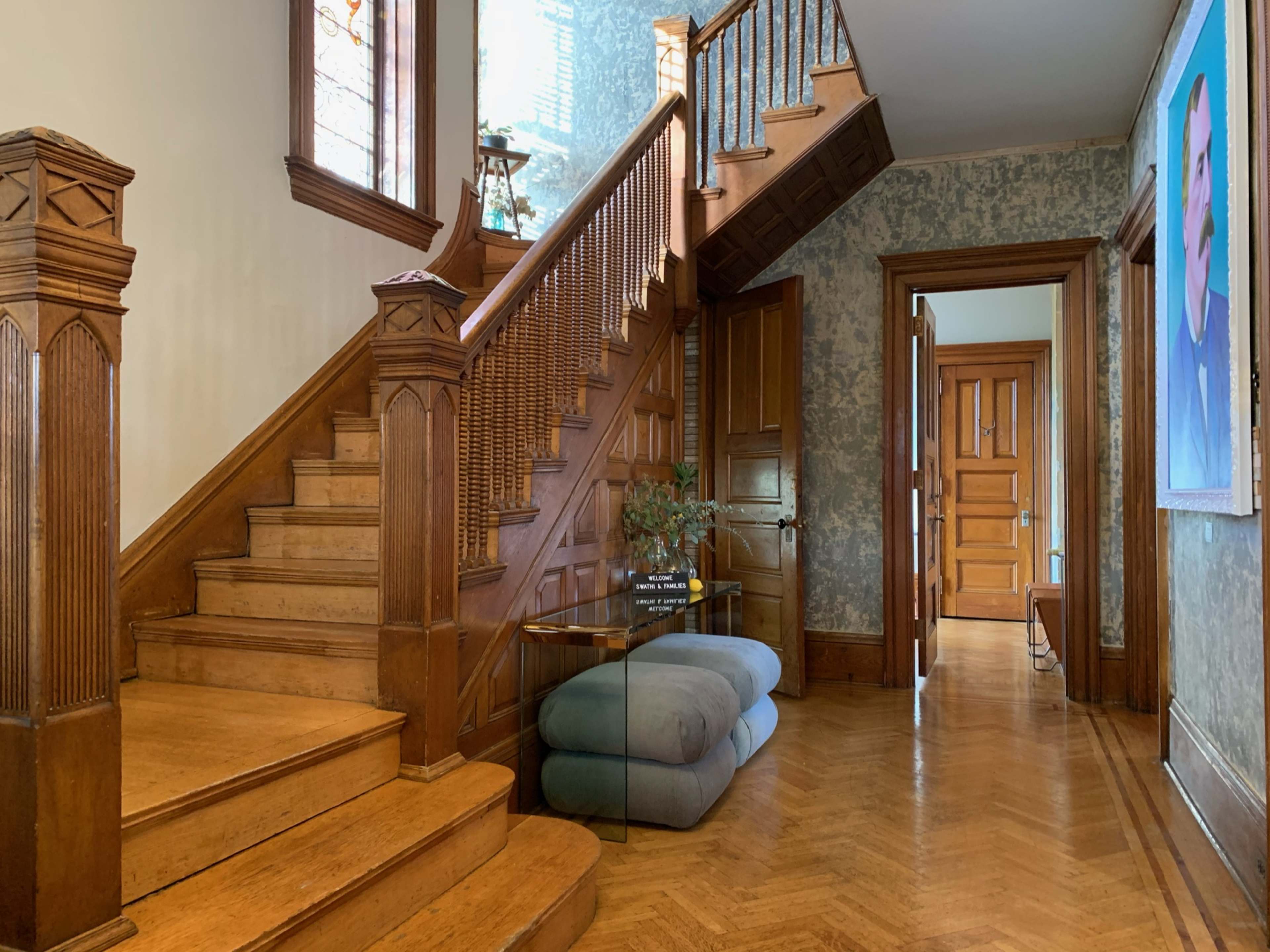 A wooden staircase in a foyer with a glass console table and a doorway leading to another room.
