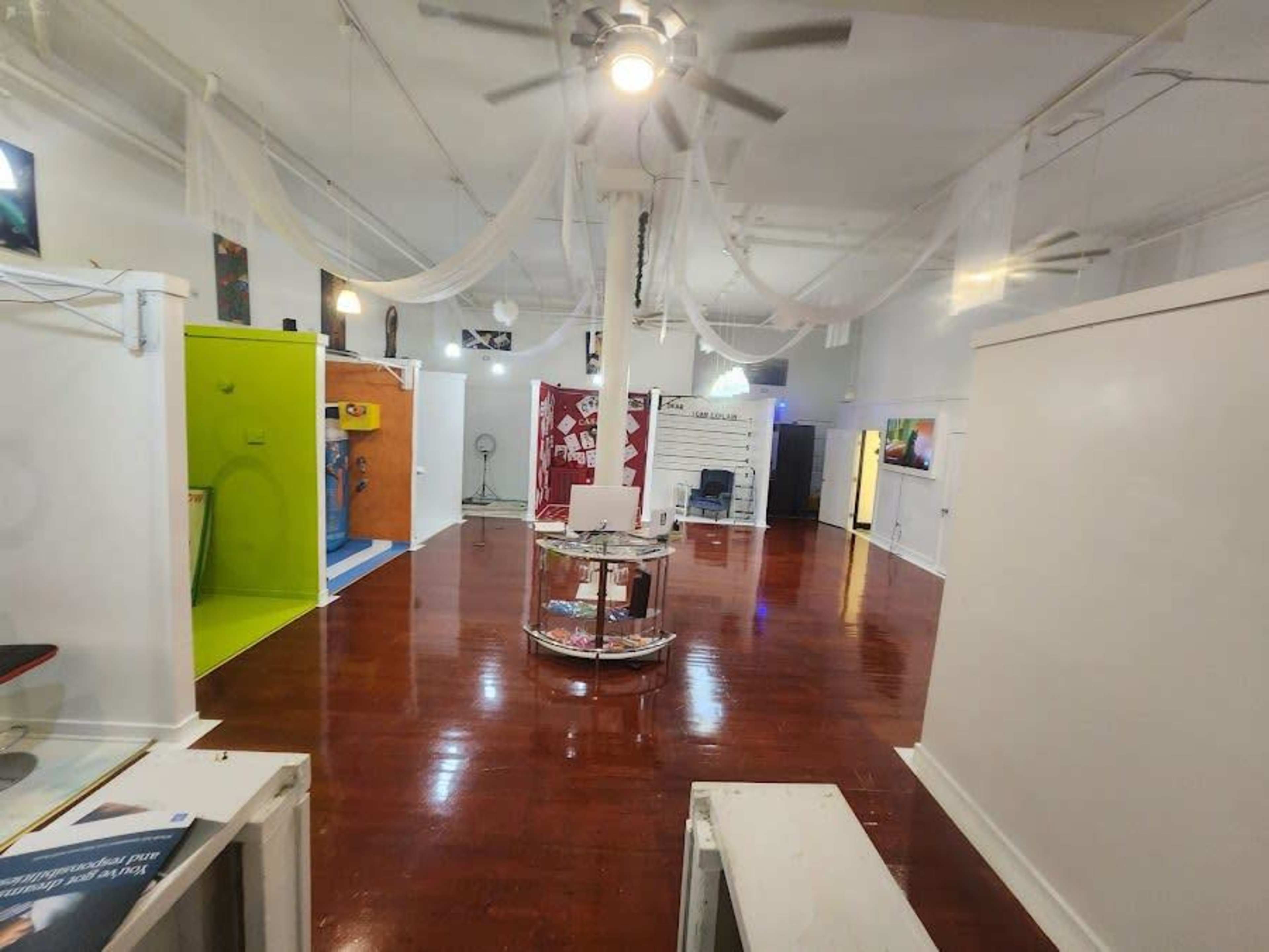 A spacious, modern gallery with white walls, polished wooden floors, and various enclosed display areas.