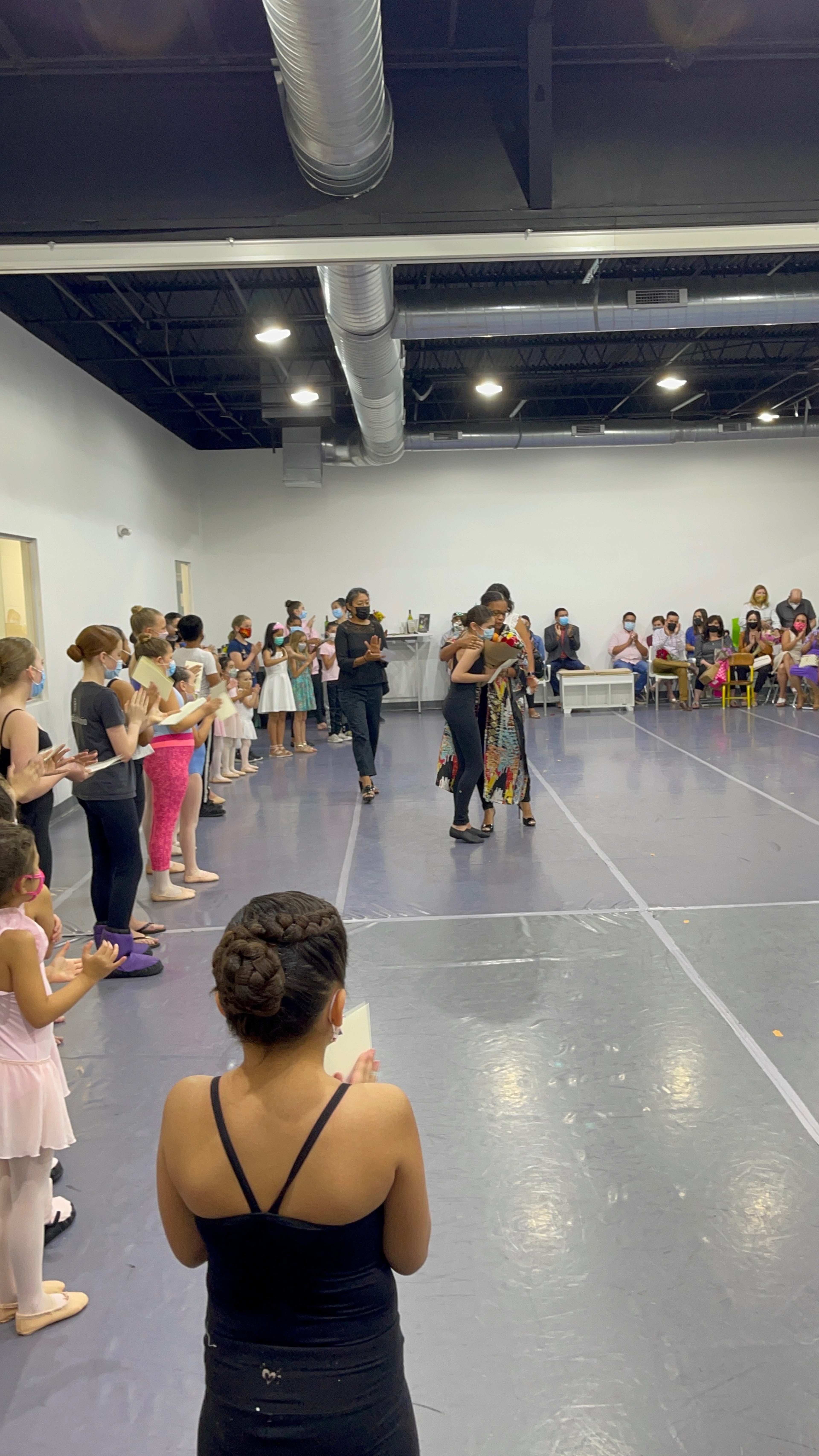 A group of dancers and spectators gather in a studio for a performance or event, with some individuals applauding while others watch.