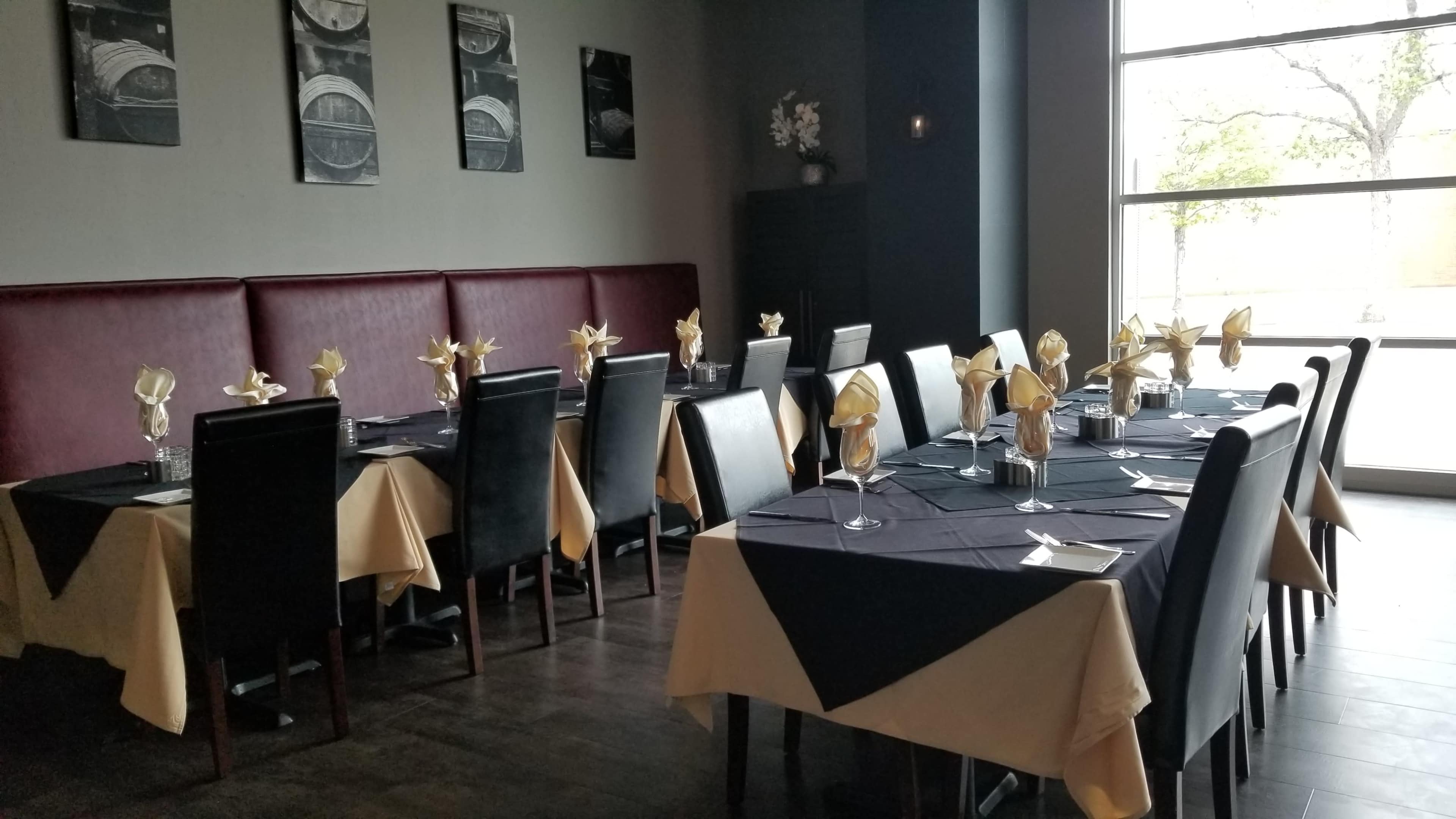 A dining area in a restaurant features neatly arranged tables covered with black and beige tablecloths, each decorated with folded napkins and glassware.