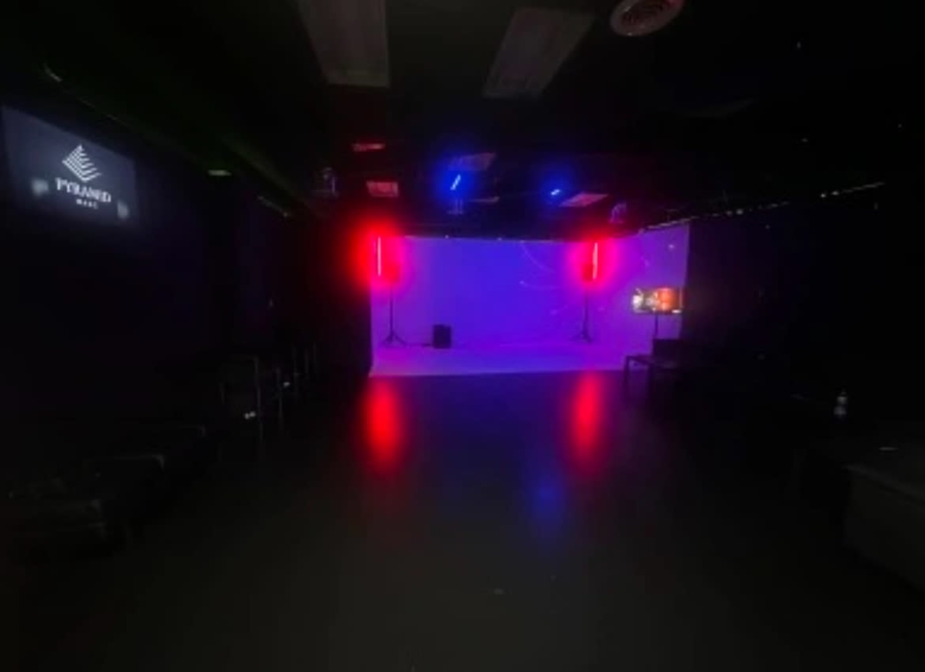 The image shows a dimly lit studio space with a bright purple backdrop and red lighting, featuring a small stage area.
