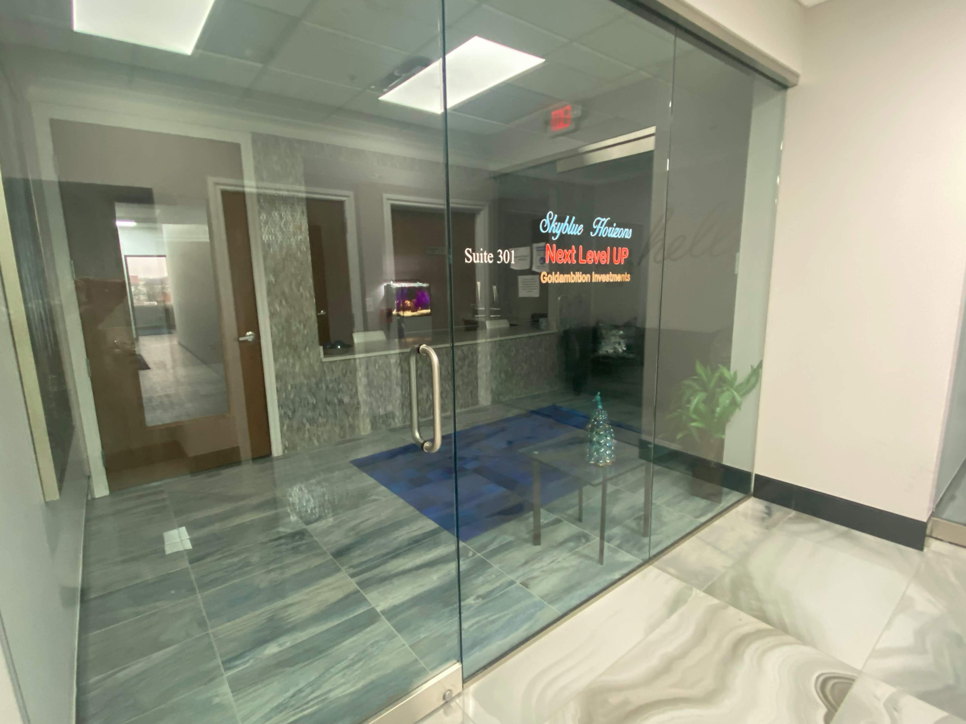 A glass entrance to an office suite labeled "Suite 301" with the text "Next Level Up" on the door, featuring a small indoor plant near the entrance.