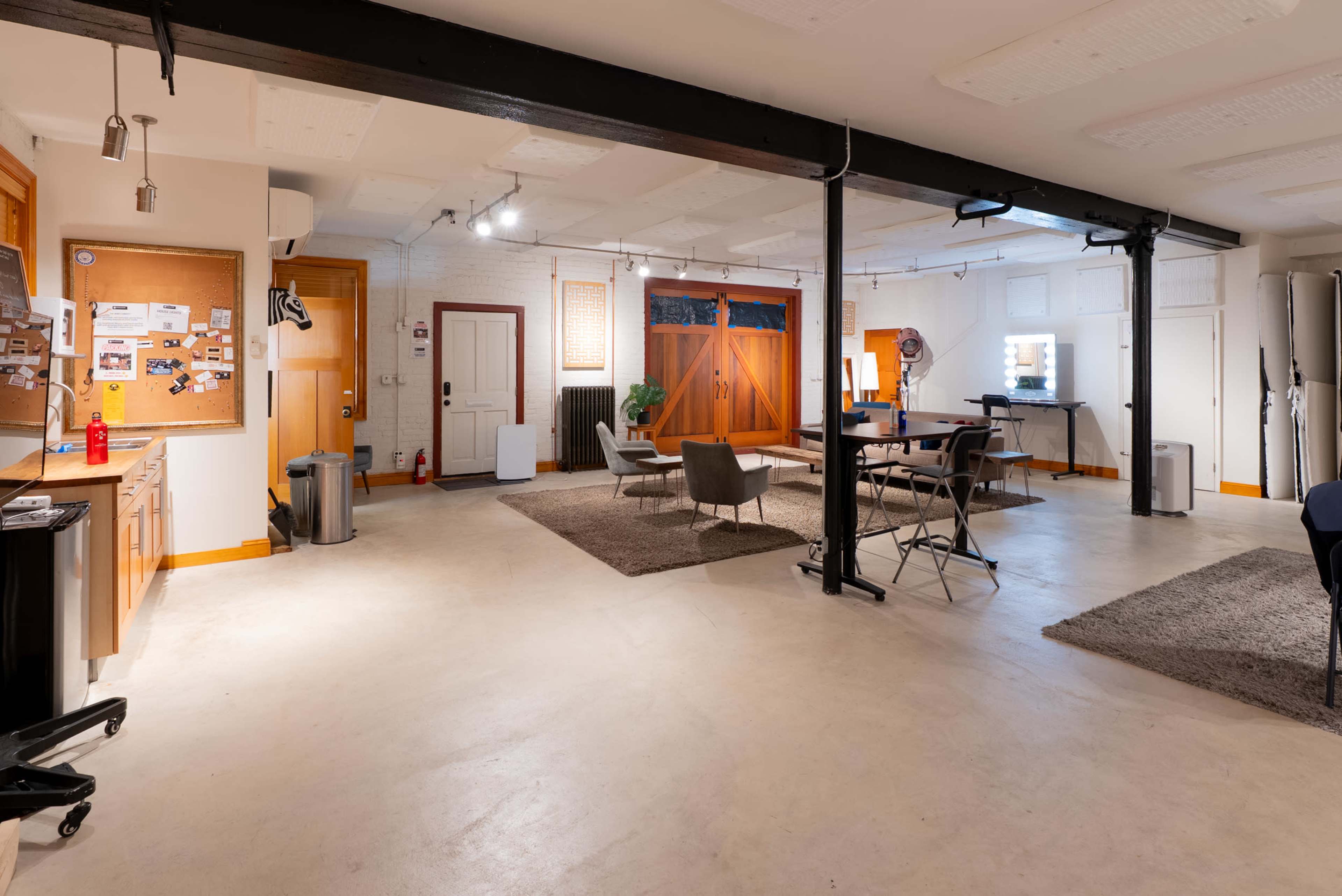 The image shows a spacious indoor area with a concrete floor, featuring a kitchen space, seating arrangements, and large windows.