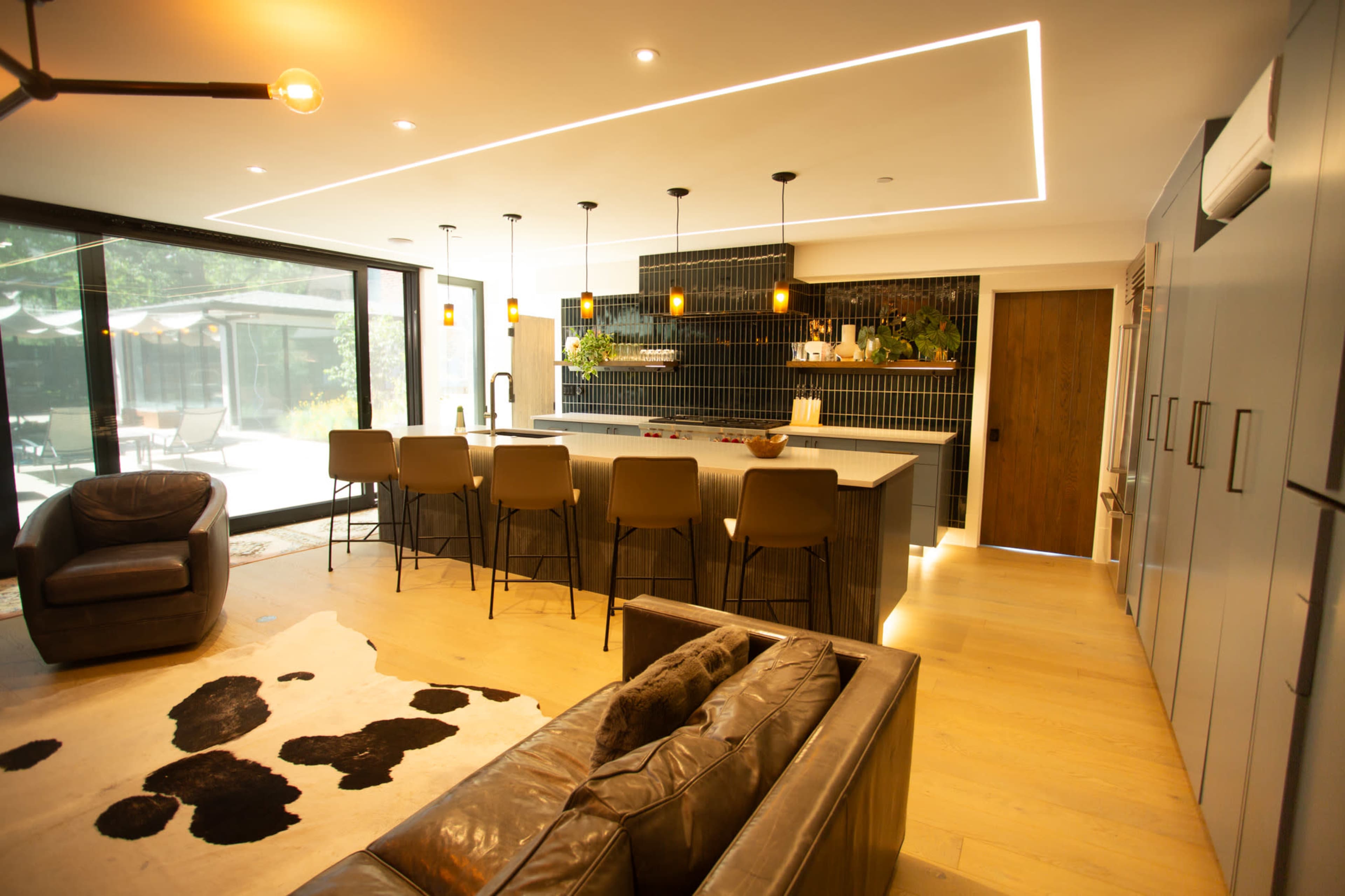 The image shows a modern kitchen with a large island, bar seating, and large glass doors leading to an outdoor area.