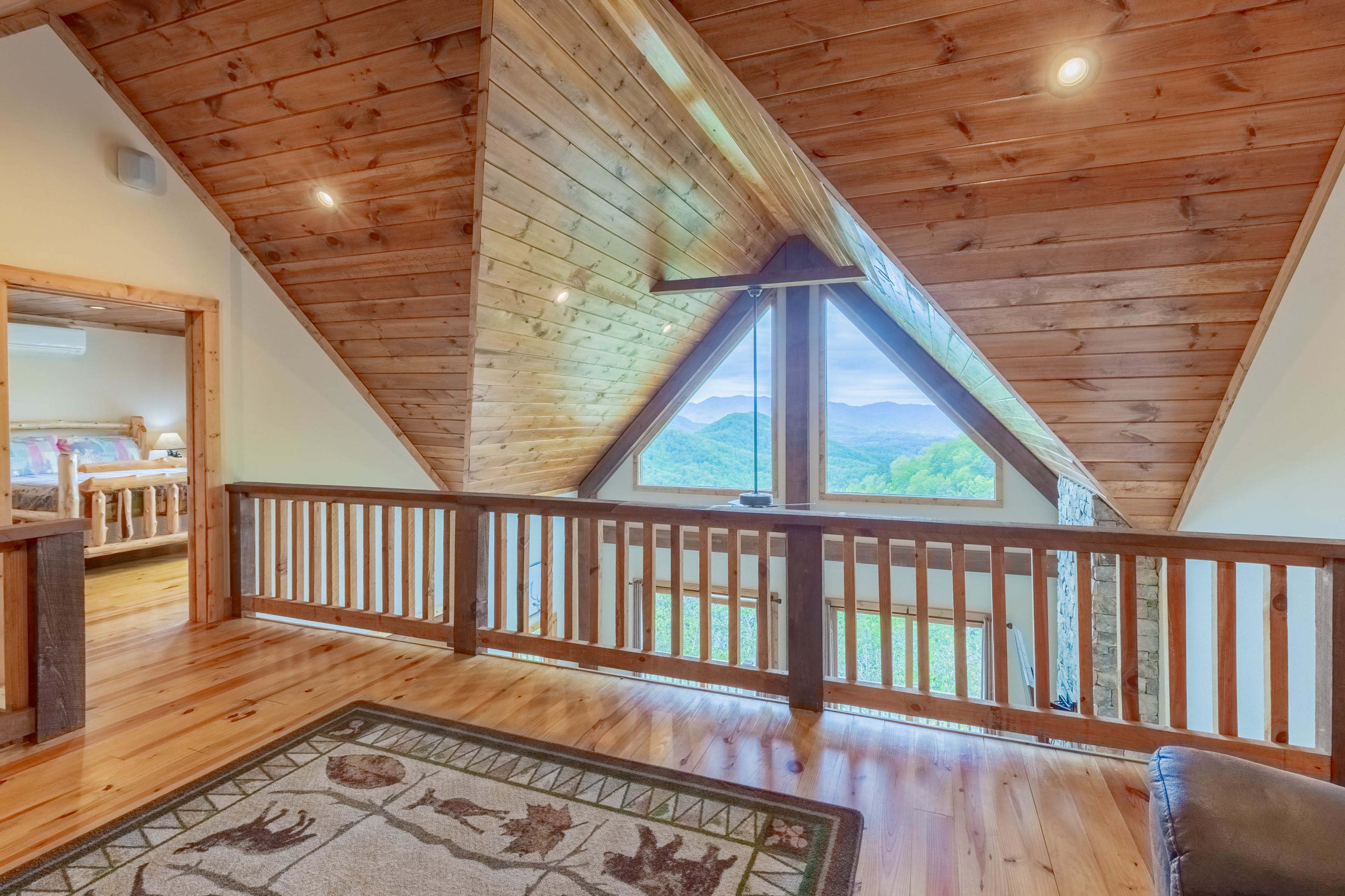 A wooden loft area with triangular windows overlooking a mountainous landscape.