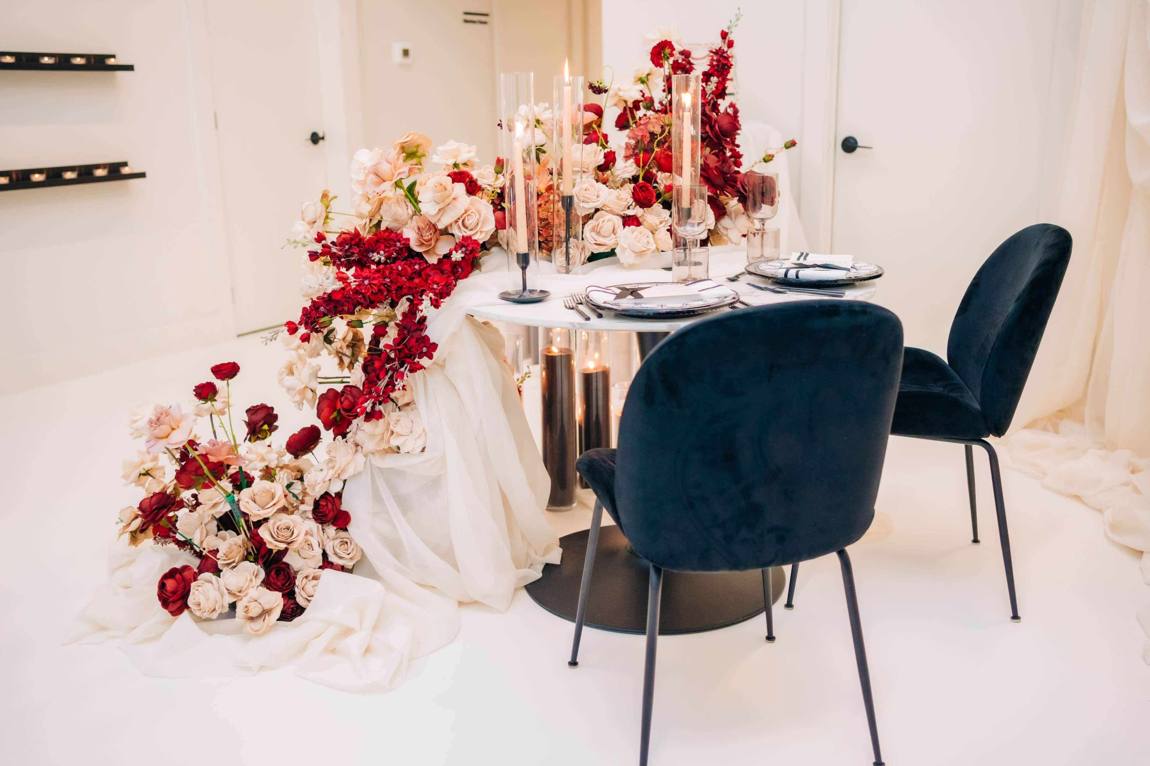 A round table elegantly decorated with an arrangement of roses and other flowers, complemented by black velvet chairs and candlelight.