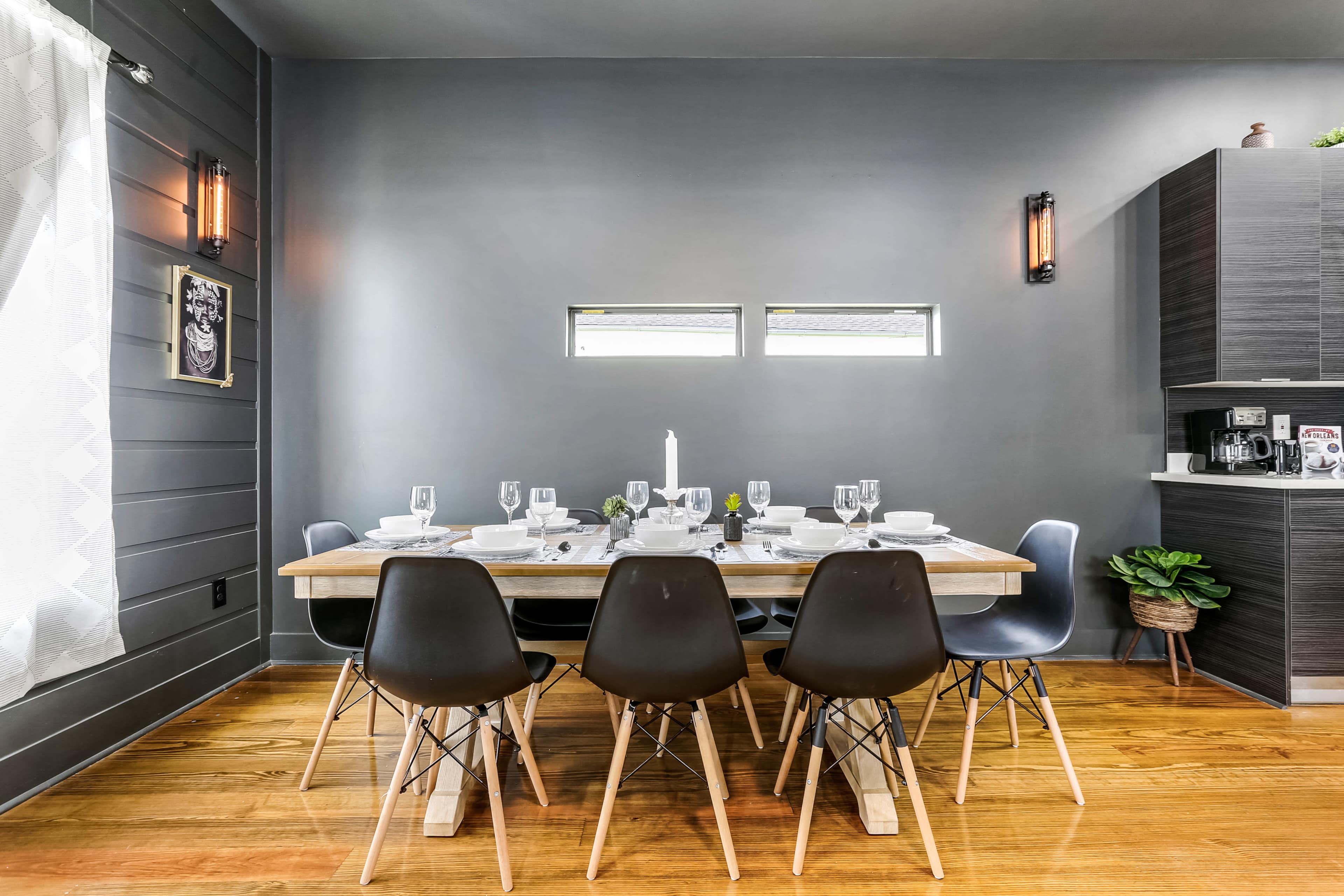 A dining table is set with plates and glassware, surrounded by chairs in a room featuring gray walls and minimal decor.