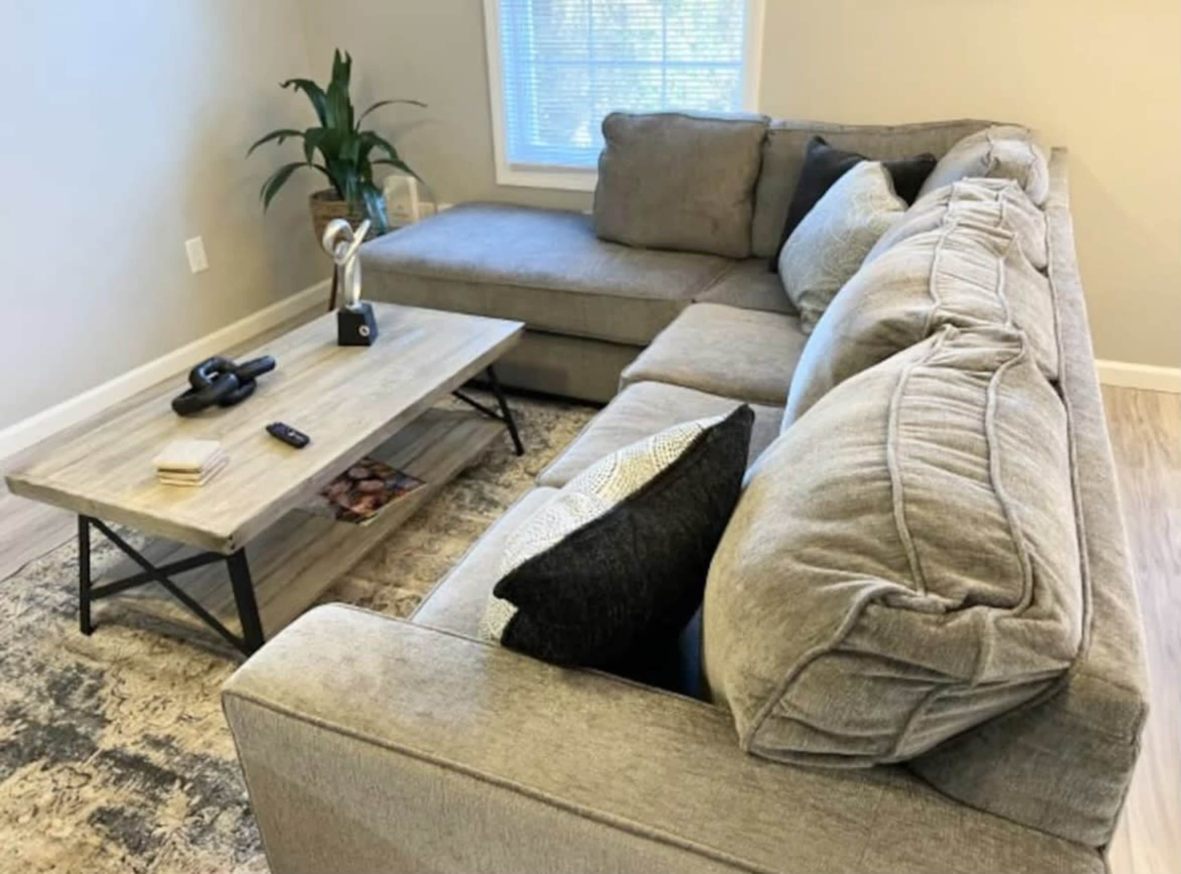 A gray sectional sofa with several pillows, positioned next to a wooden coffee table in a well-lit living room.