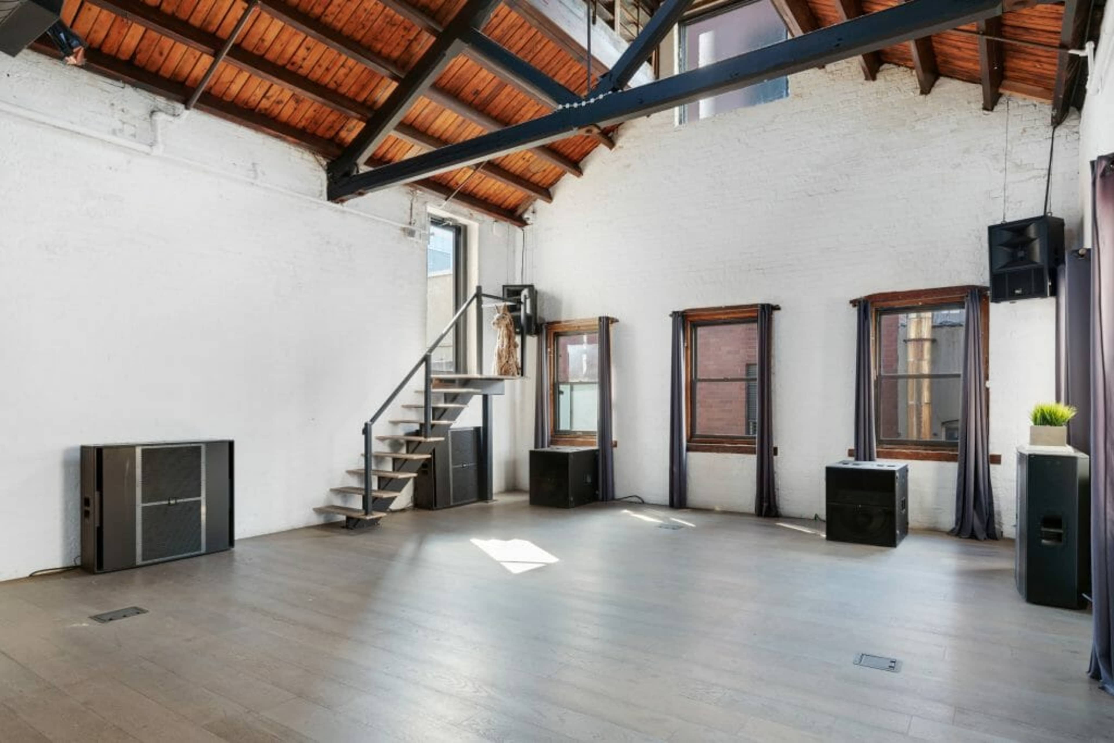 A spacious room with wooden beams, large windows, and sound equipment placed strategically around the perimeter.