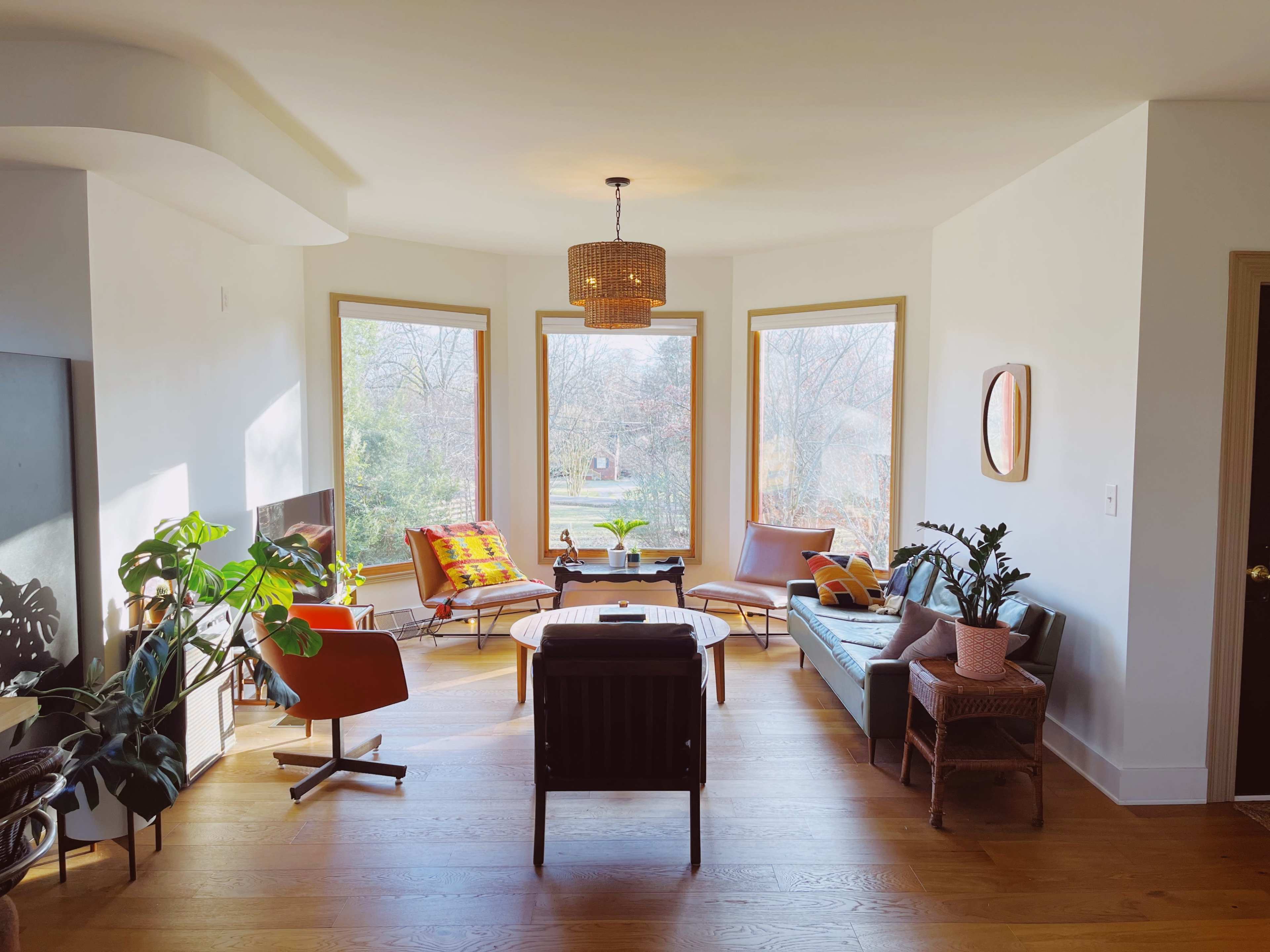 A bright living room with large windows, featuring a mix of seating options, plants, and a coffee table.