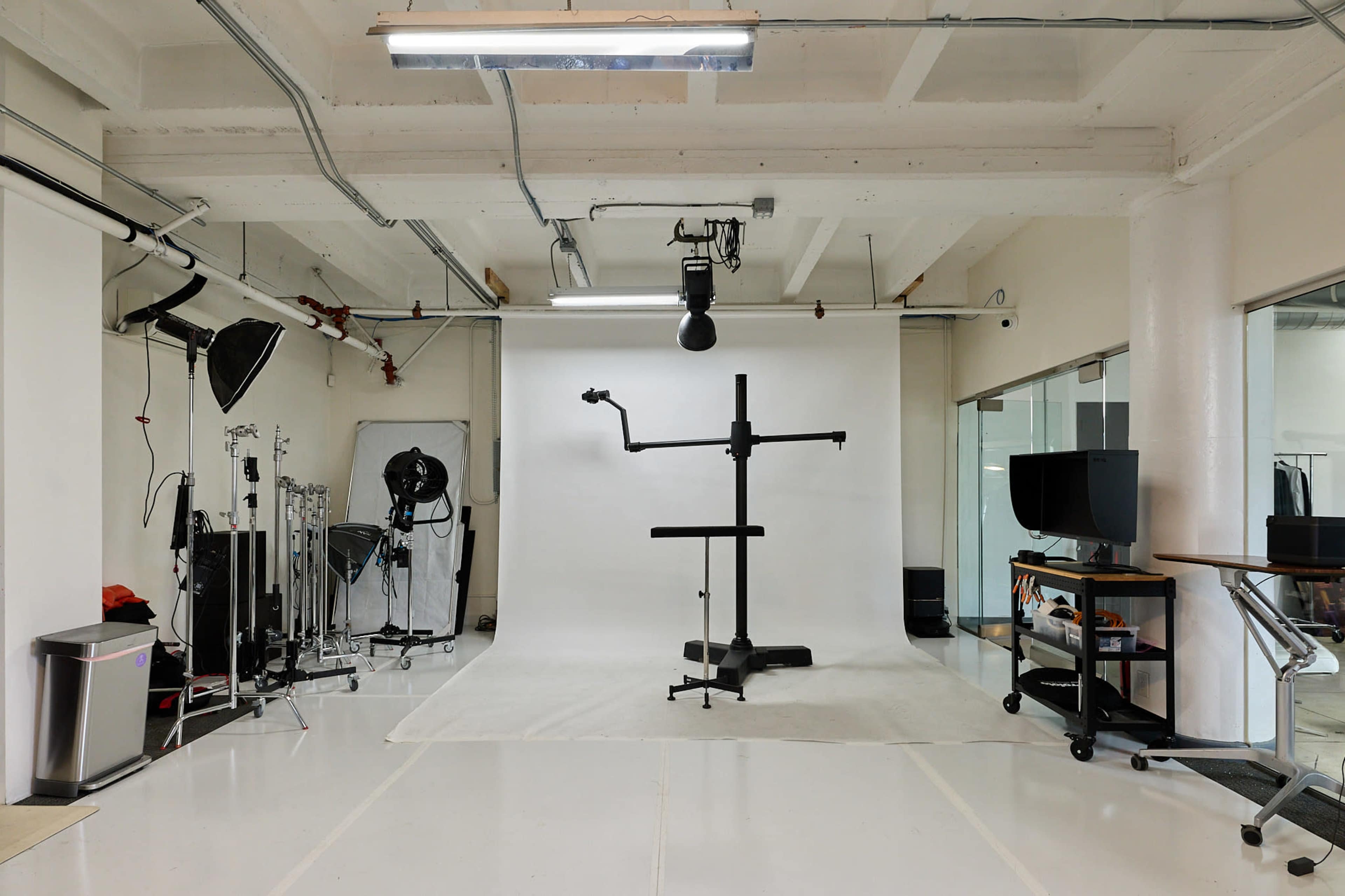 The image shows a spacious photography studio with a white backdrop, studio lighting equipment, and various props arranged around the room.