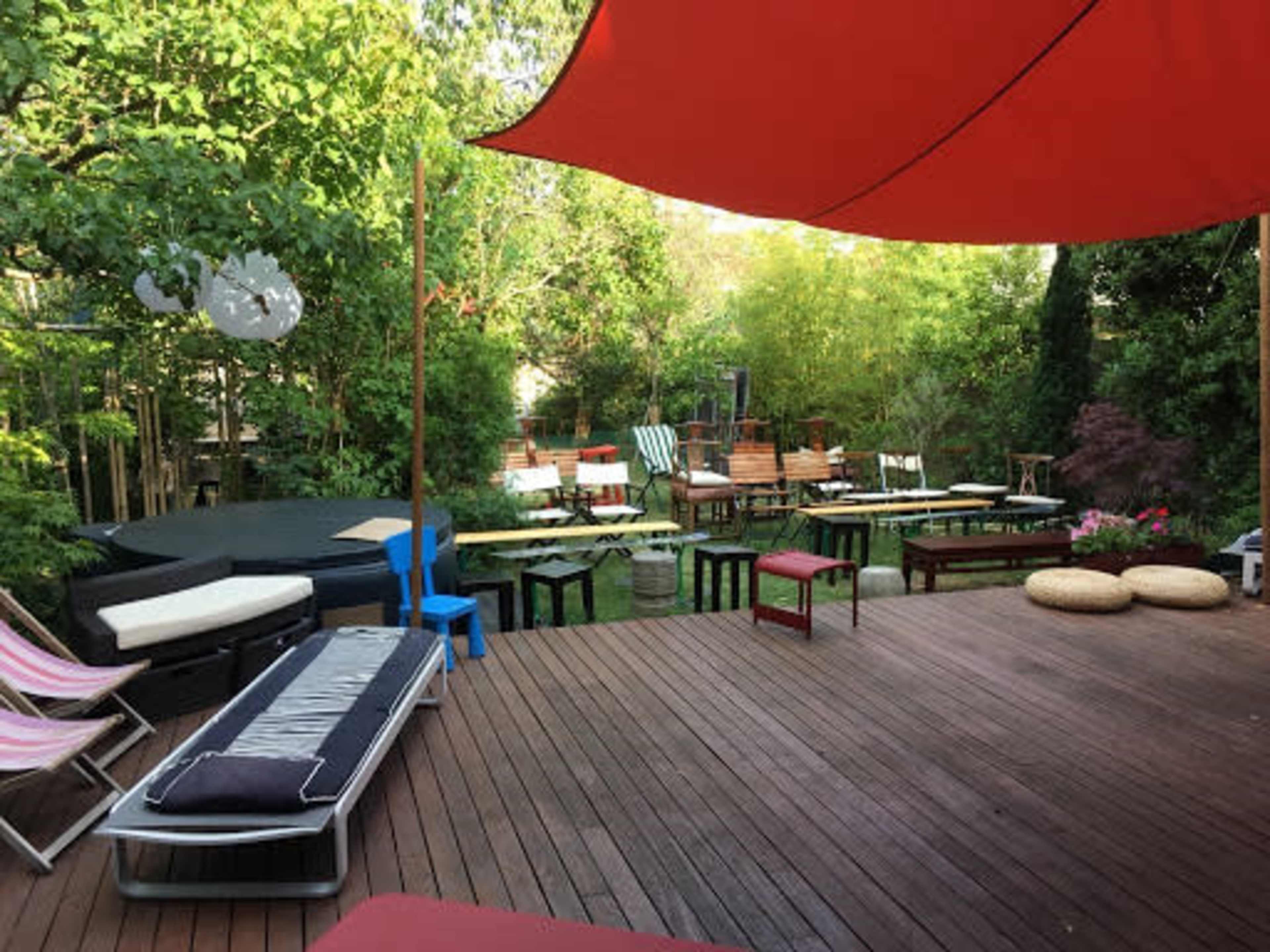 The image shows a wooden deck area with various seating options, including lounge chairs and benches, surrounded by greenery.