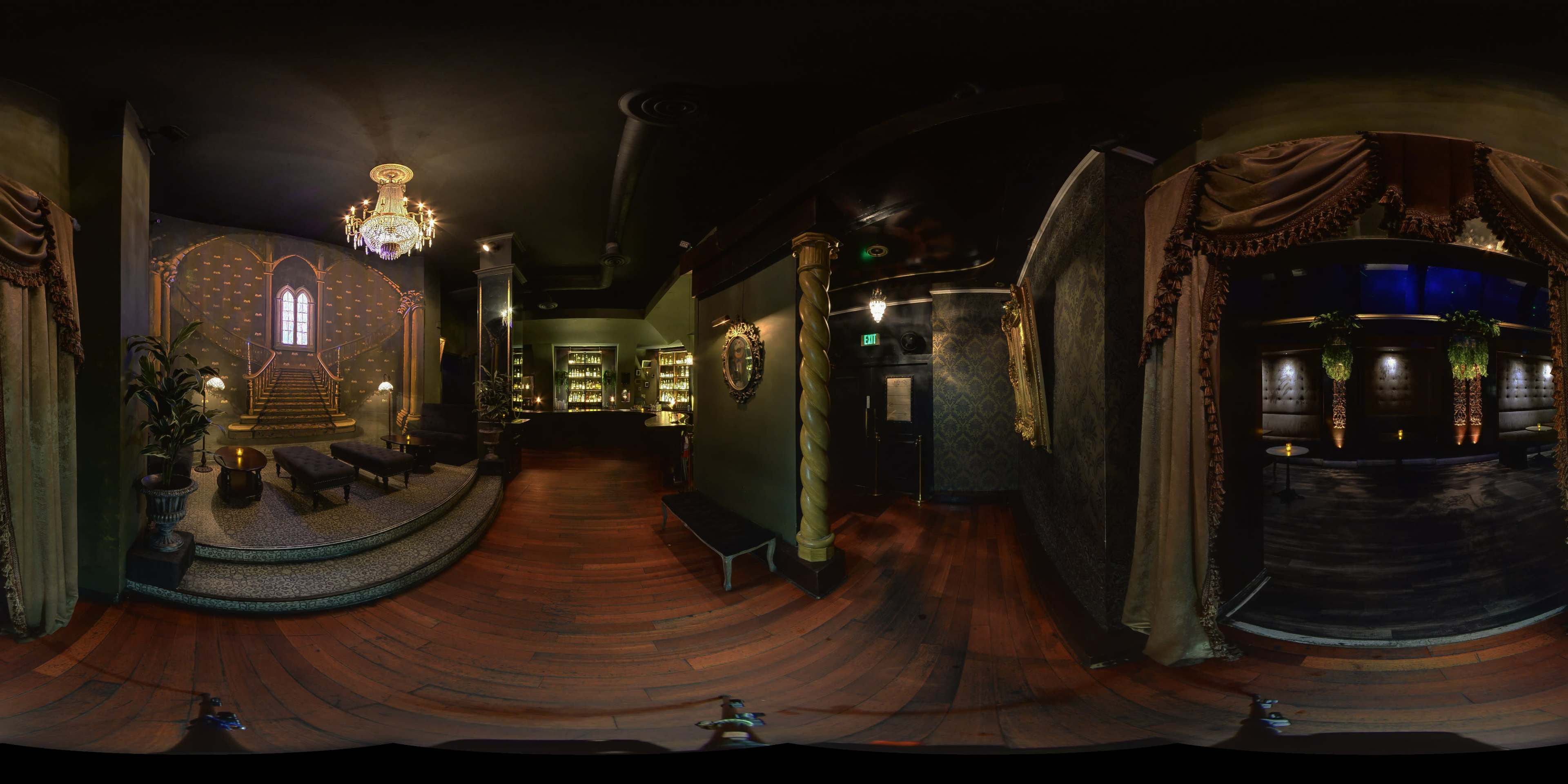 A dimly lit, elegantly designed interior with plush seating, ornate decor, and a decorative staircase leading to a prominent window.