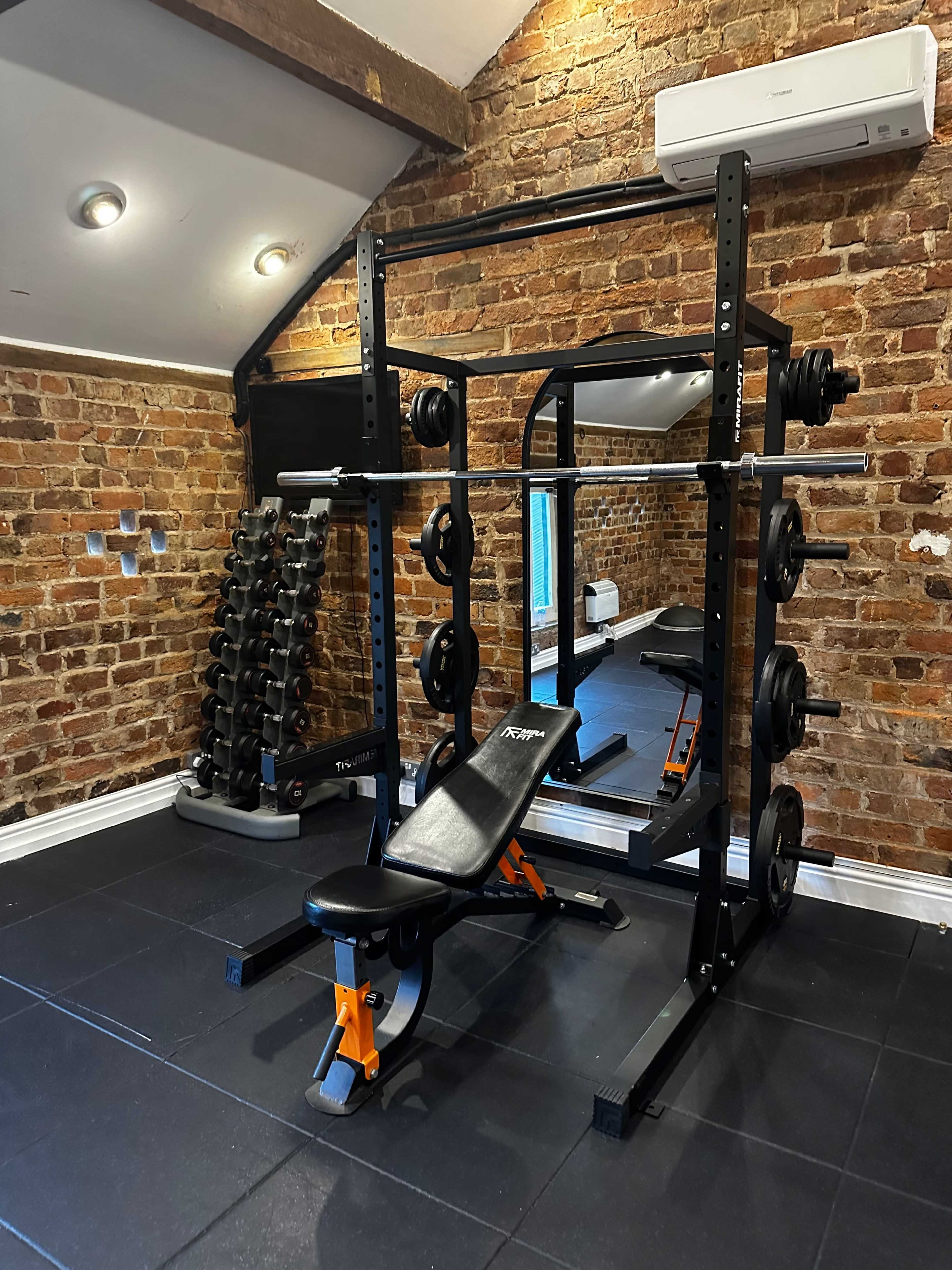 A home gym with a weight rack, free weights, a bench press, and exposed brick walls.