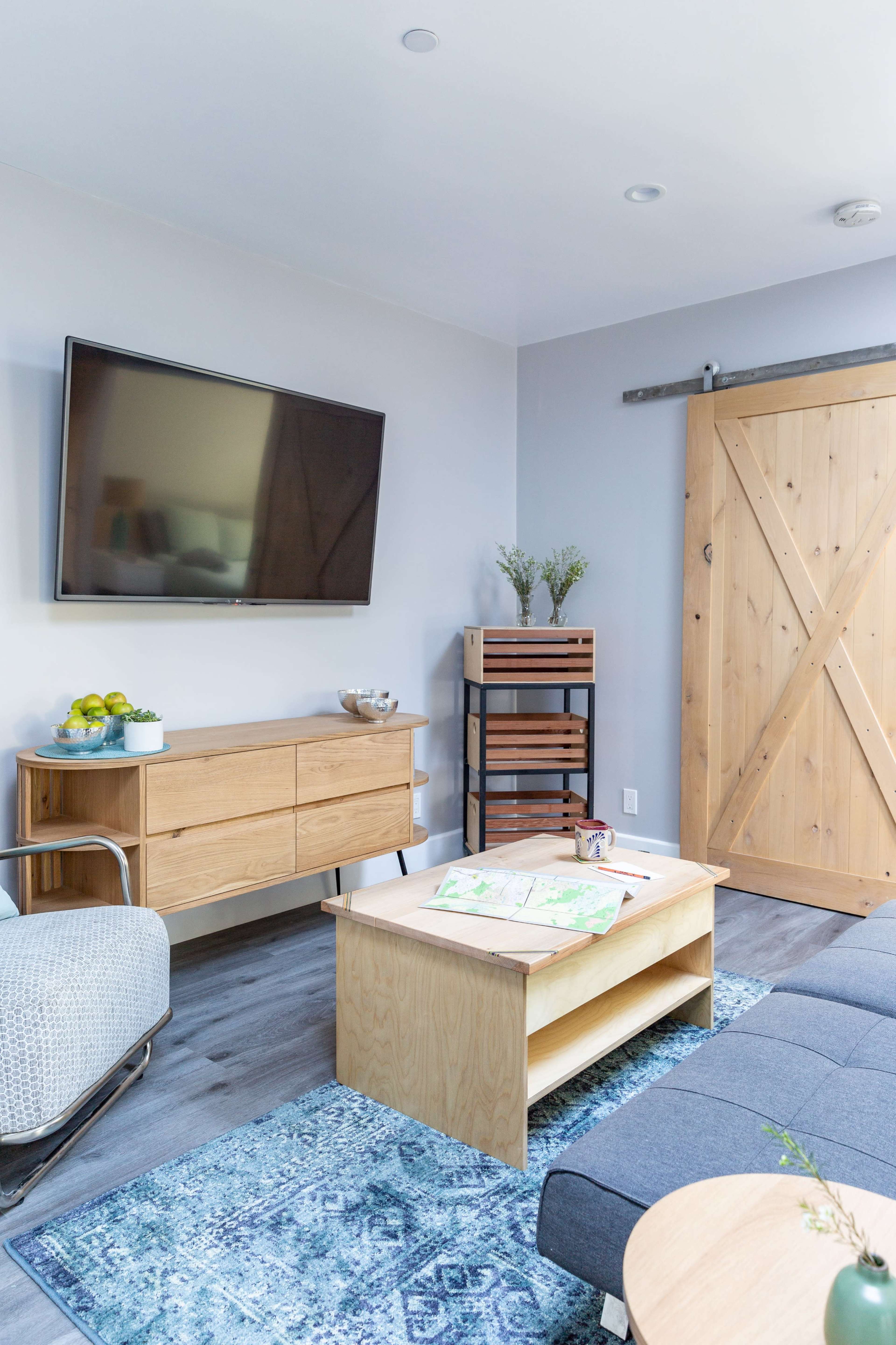 The living room features a flat-screen TV mounted on the wall, a wooden sideboard, a coffee table with a map, and a sliding barn door.