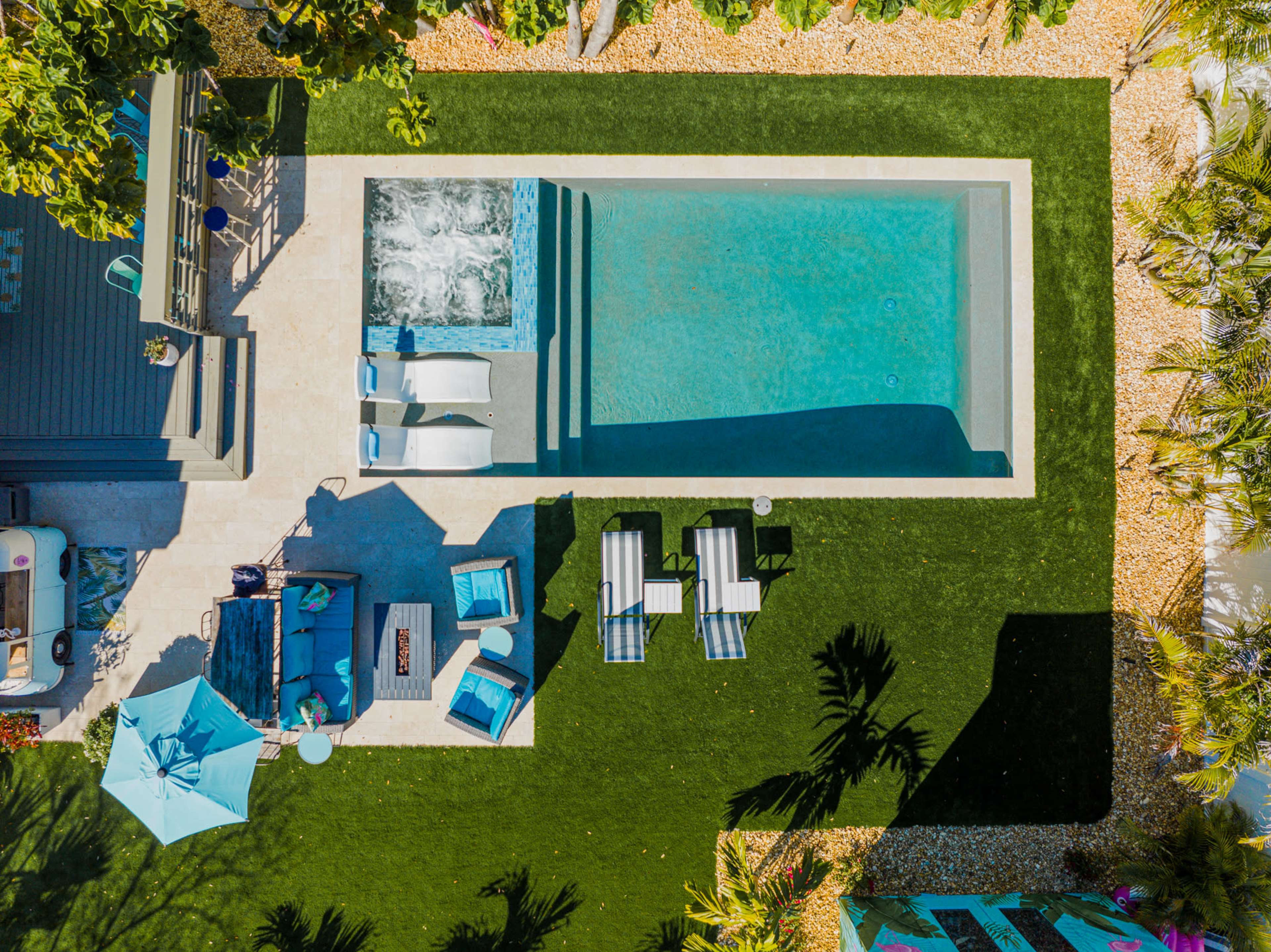 An aerial view of a backyard featuring a swimming pool, lounge chairs, and a seating area surrounded by manicured grass and landscaping.