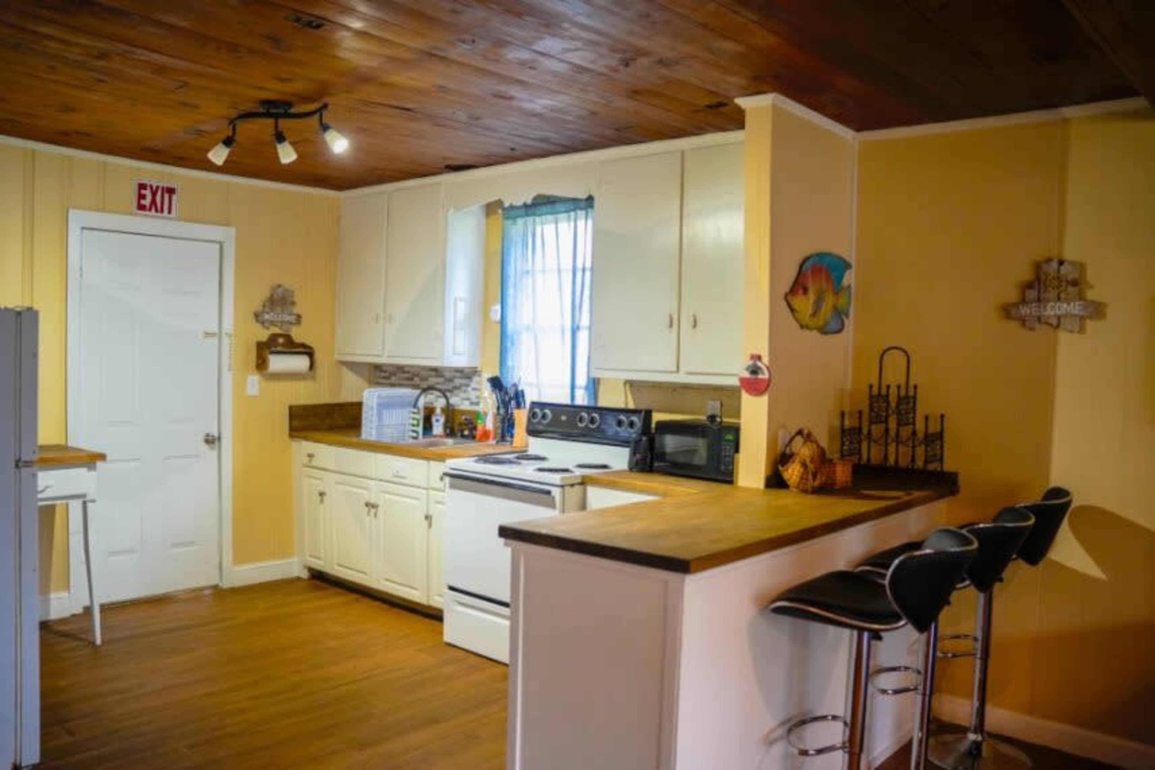 A kitchen with white cabinets, a wooden countertop, and a bar with three black stools.