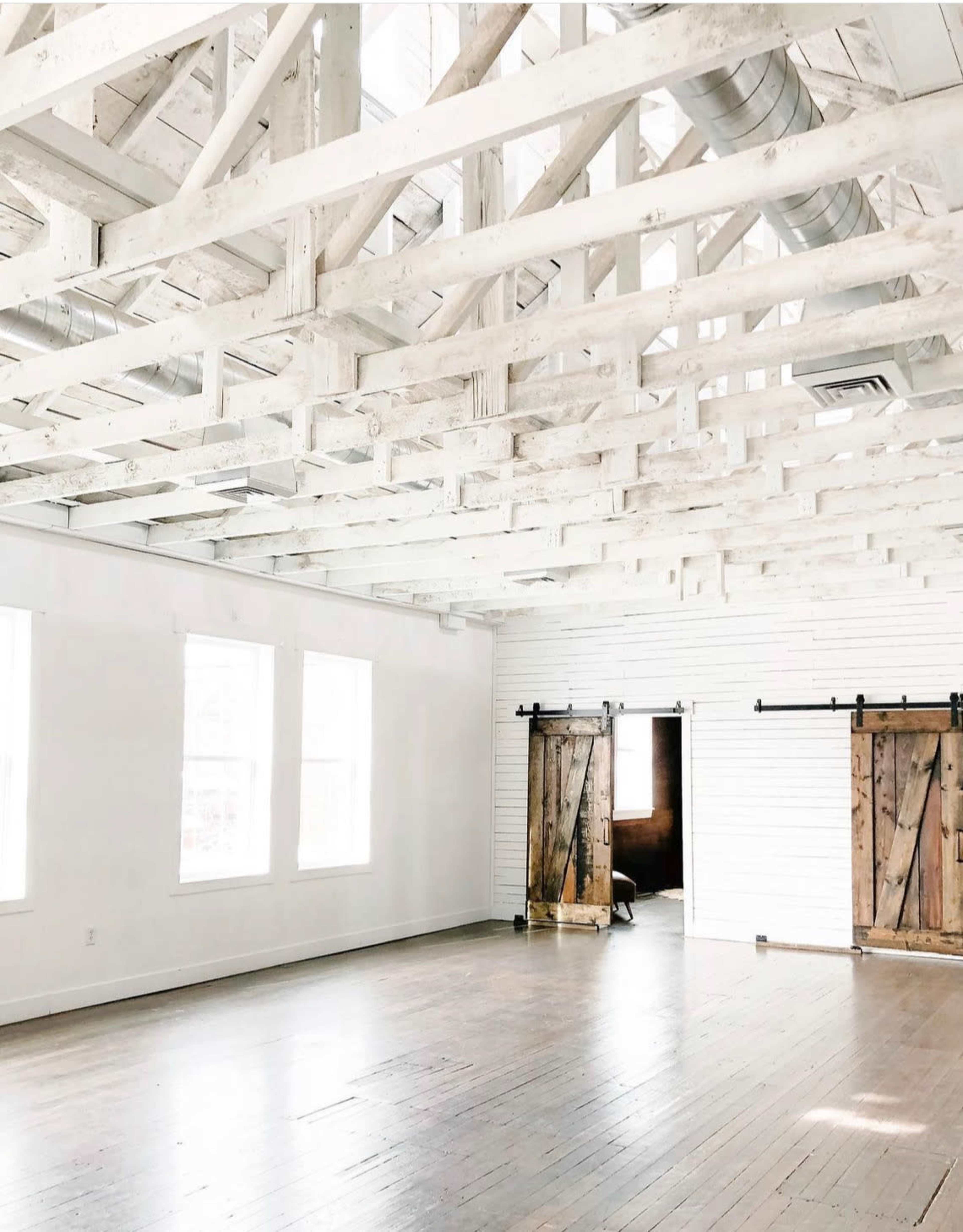A spacious room with a white wooden ceiling and two large barn-style doors on opposite sides.