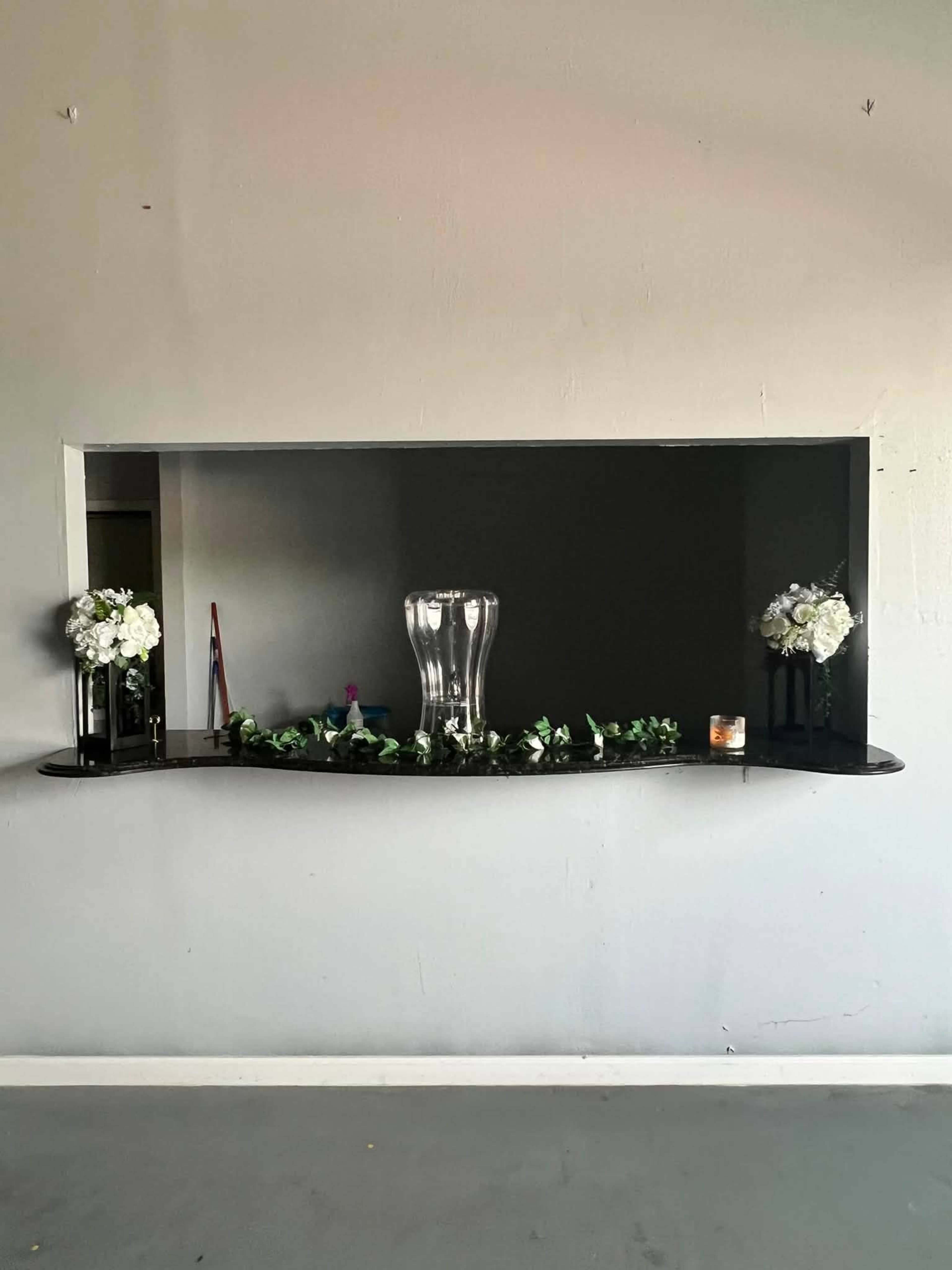A wall-mounted shelf displays a glass vase and decorative flowers against a gray background.
