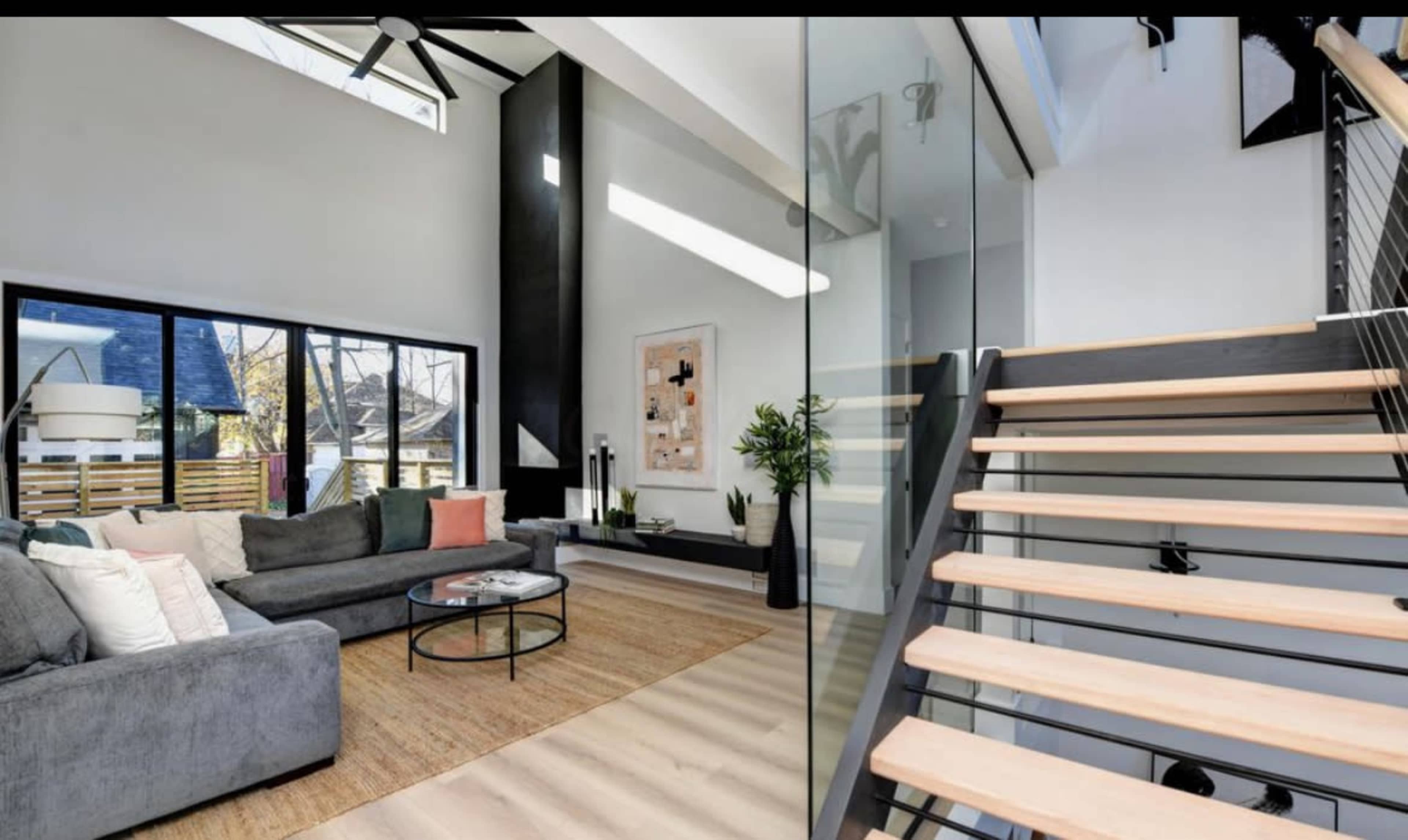 A modern living room with a gray sofa, a round coffee table, a large window, and a staircase leading to an upper level.