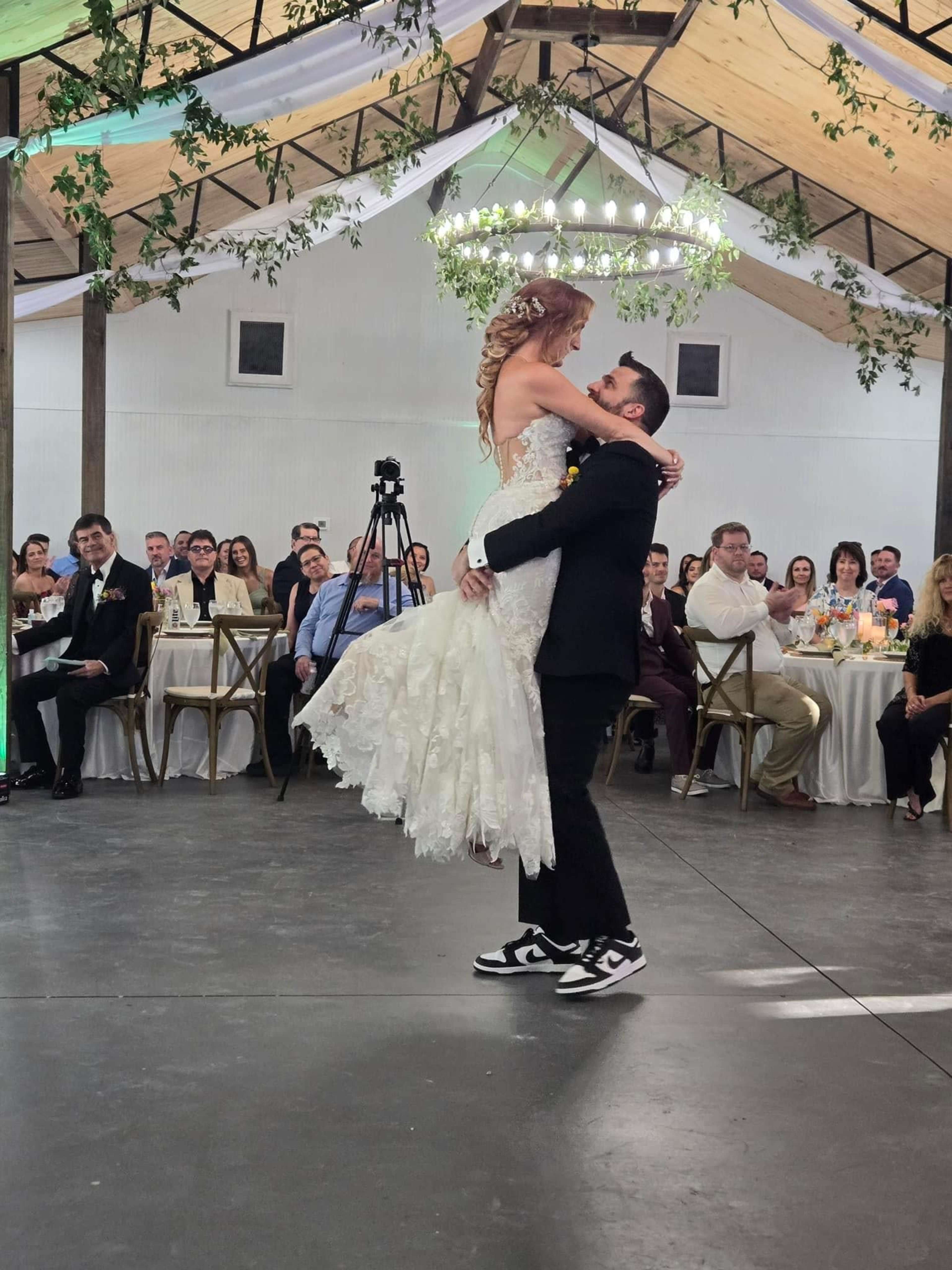 A man lifts a woman in a wedding dress in a decorated reception hall filled with seated guests.