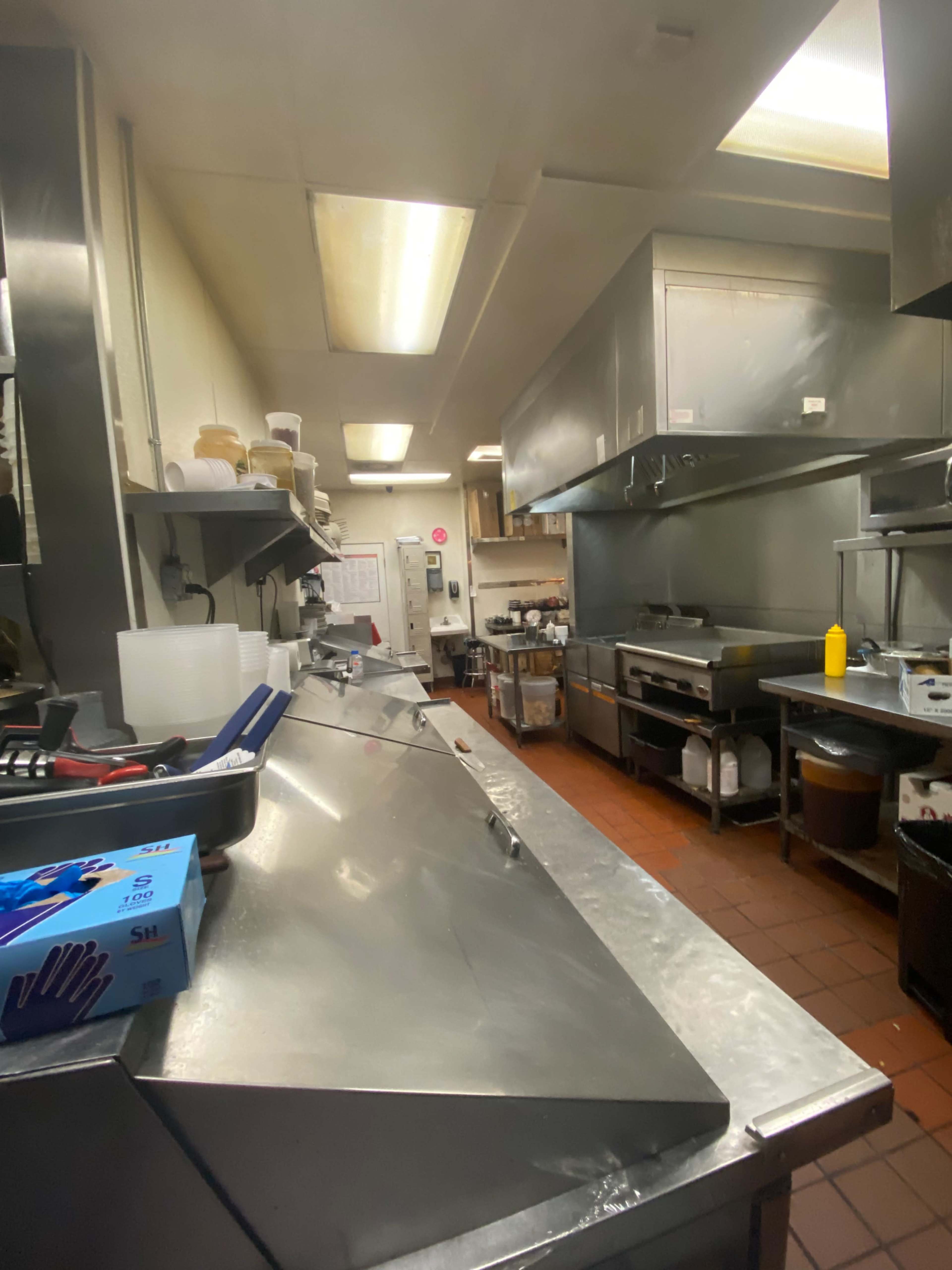 A commercial kitchen with stainless steel countertops, cooking equipment, and various utensils organized along the walls.