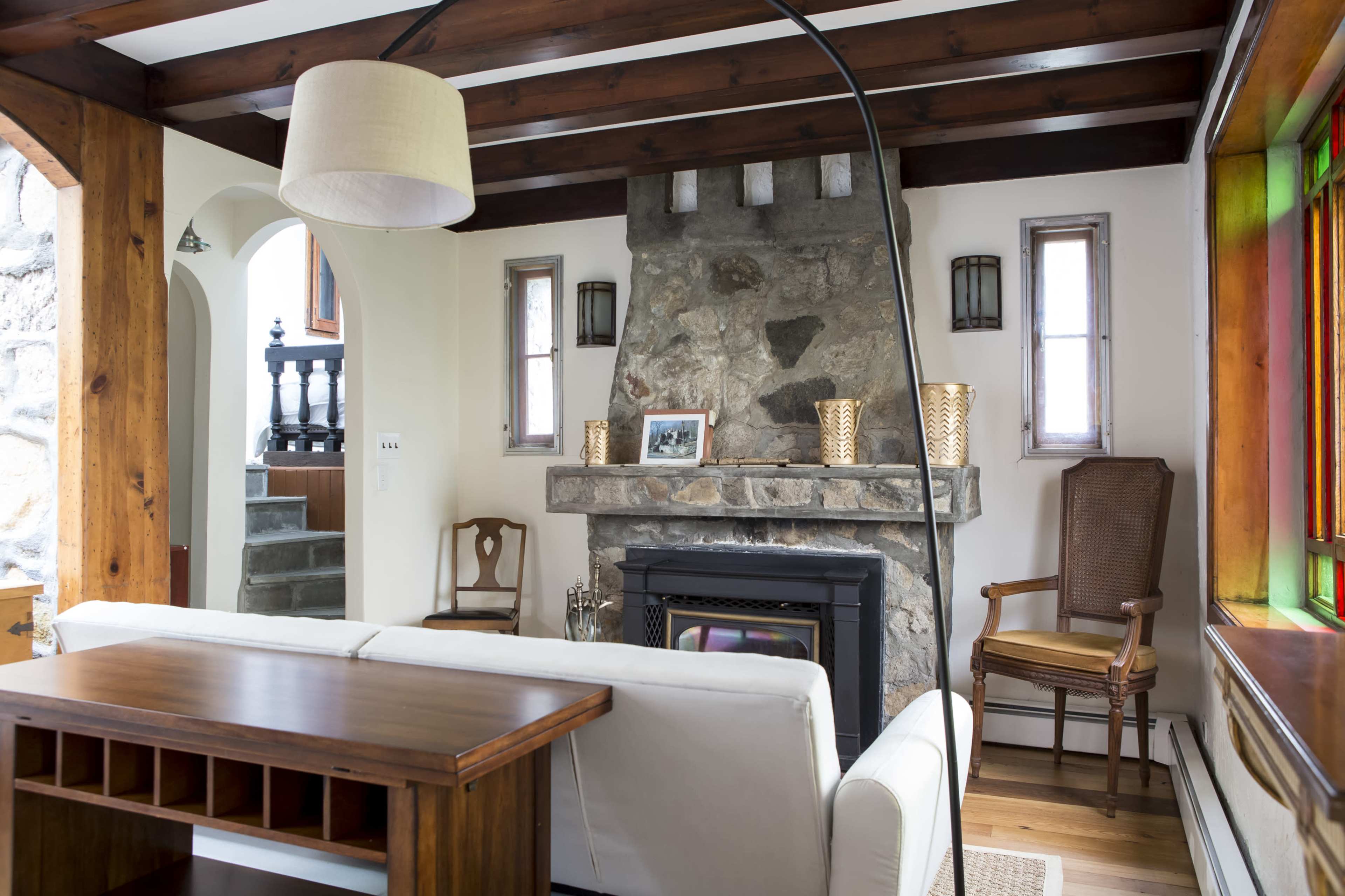 A living room with a stone fireplace, wooden beams, and a white couch facing a wood table.