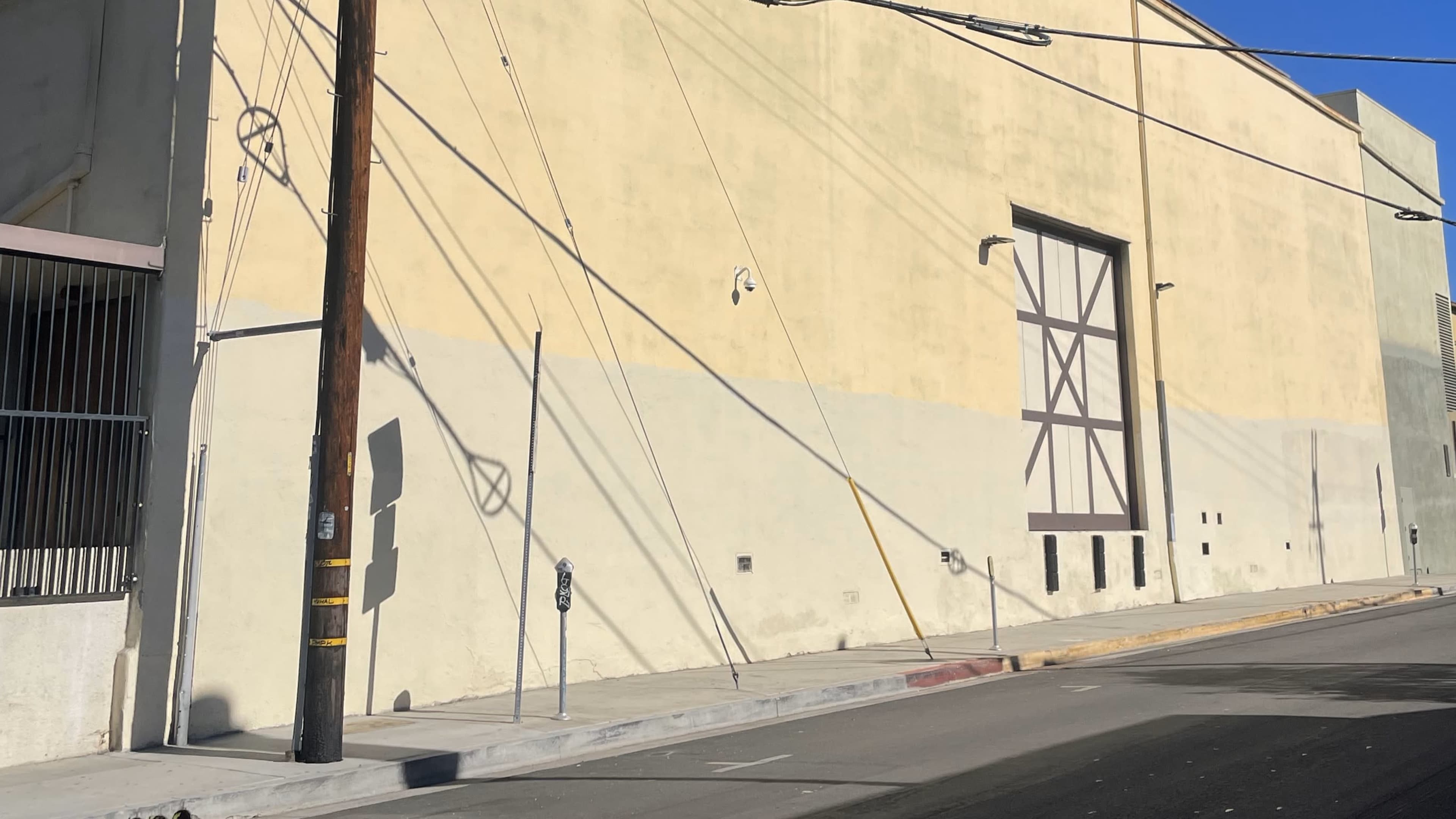 The image shows a light-colored building wall with a large door and power lines casting shadows on the surface.