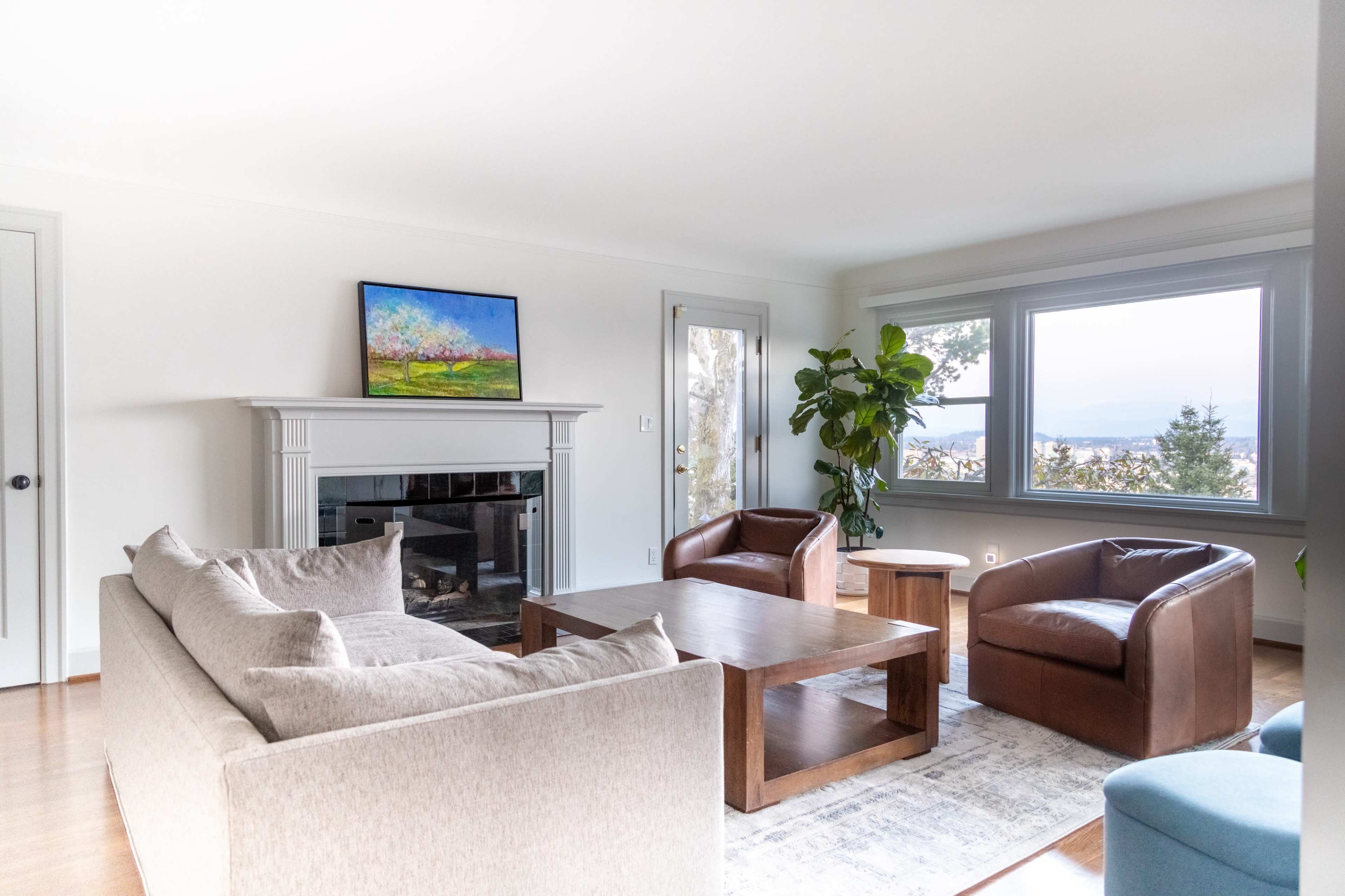 A modern living room featuring a beige sofa, two brown armchairs, a wooden coffee table, and a large window with a view.