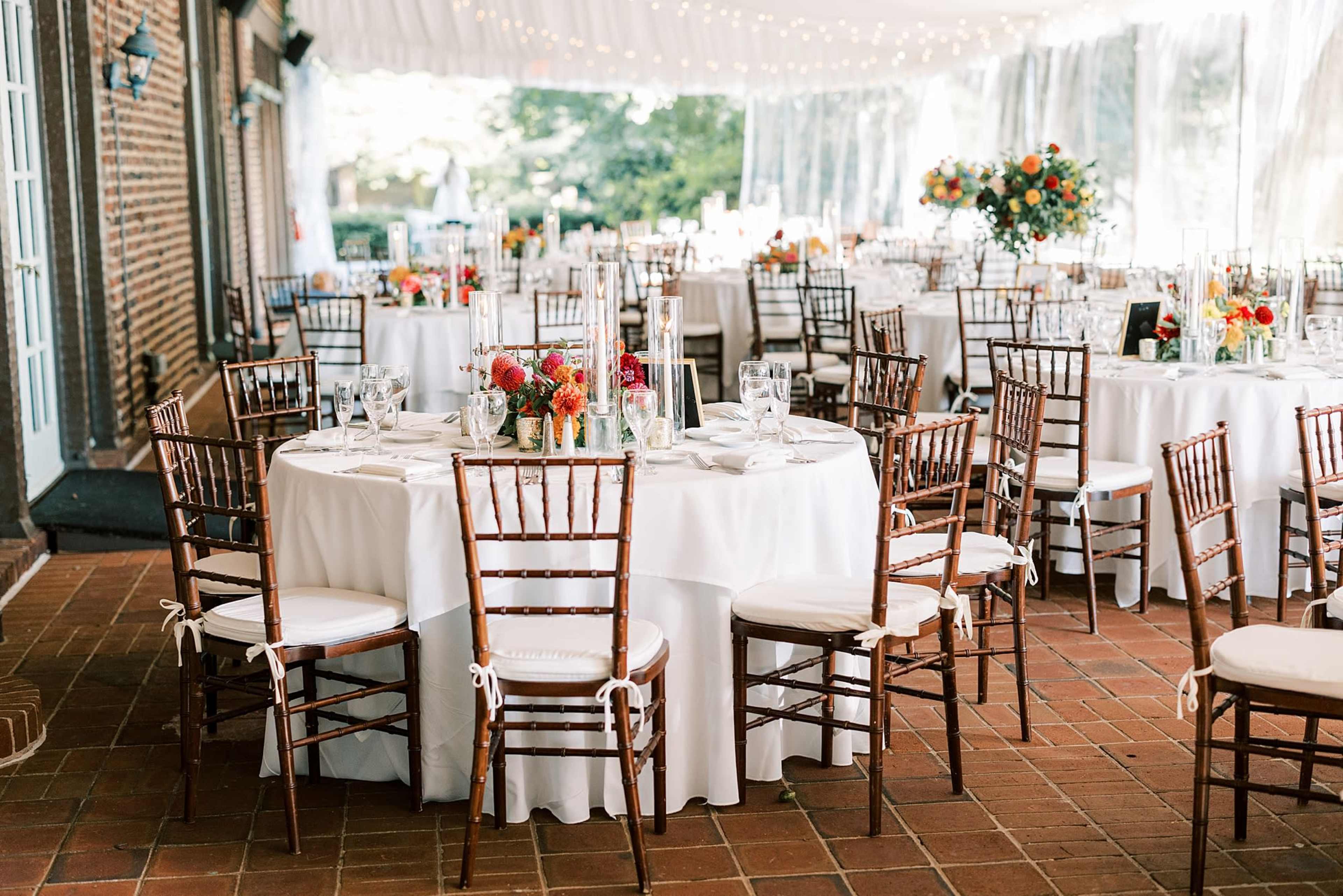 A beautifully arranged dining area with round tables covered in white tablecloths, set with floral centerpieces and surrounded by wooden chairs.