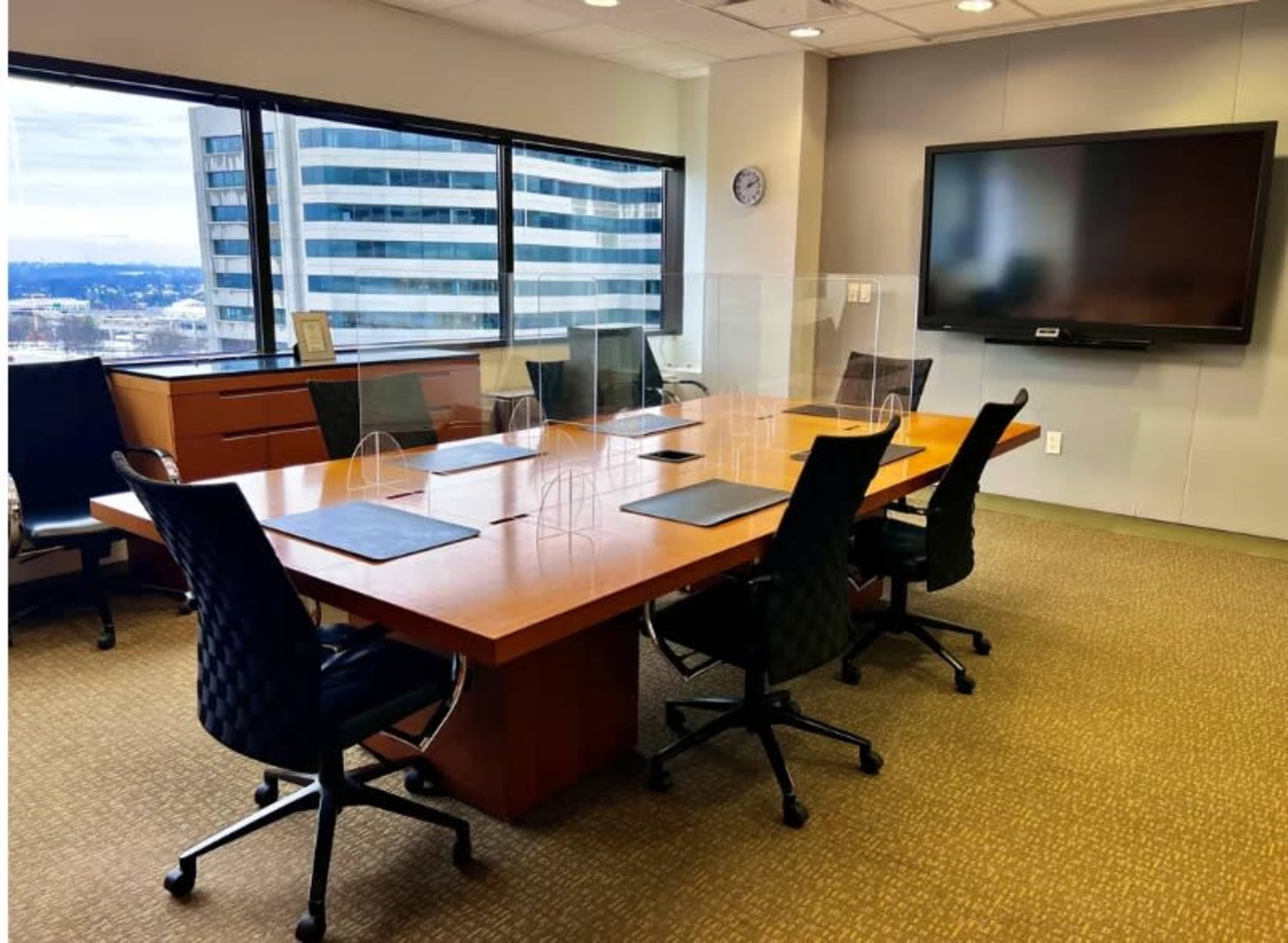 A large conference room features a rectangular wooden table surrounded by black chairs and a wall-mounted television.