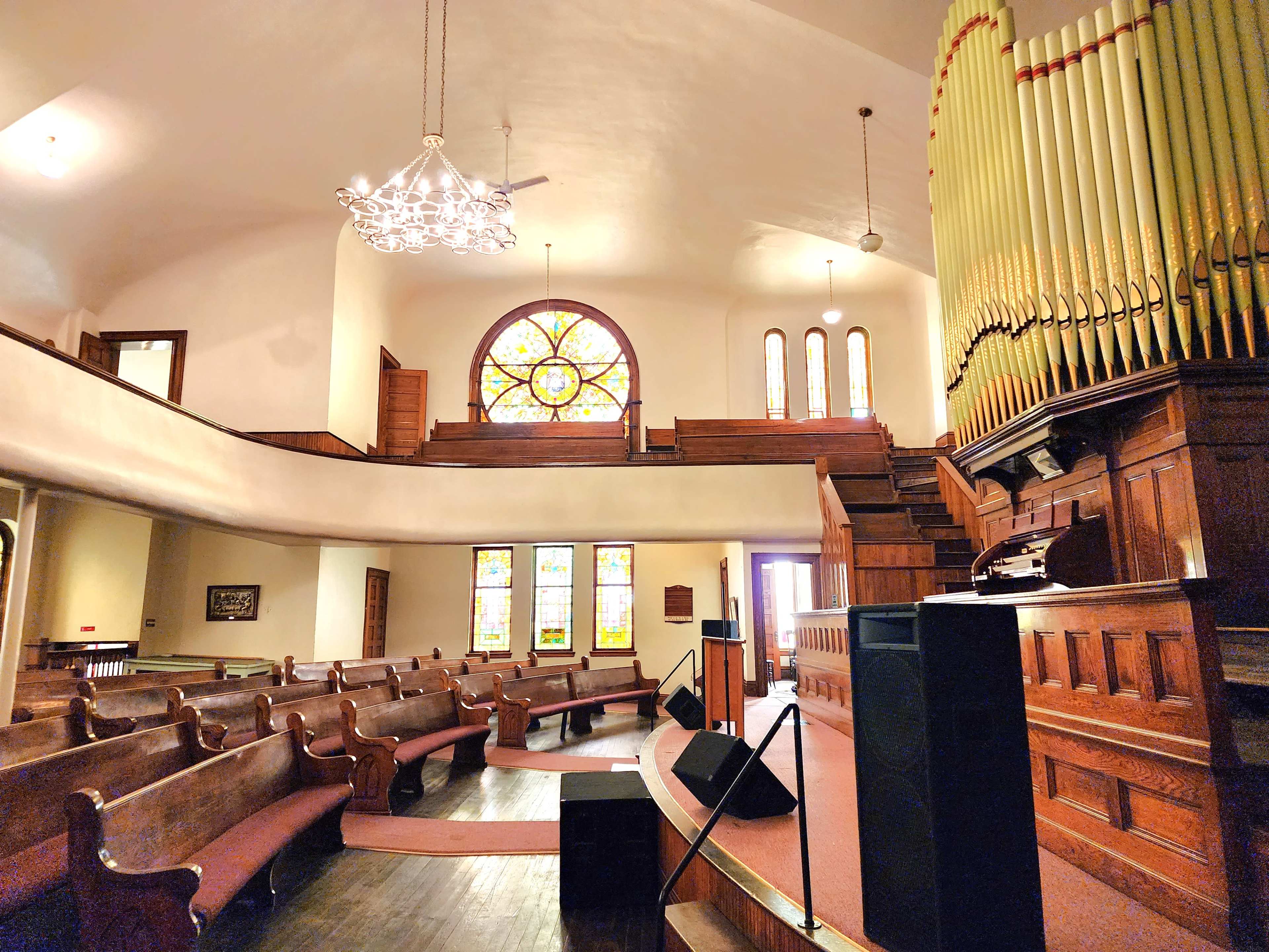 The interior of a church features wooden pews, a large organ, stained glass windows, and a flight of stairs leading to a balcony.