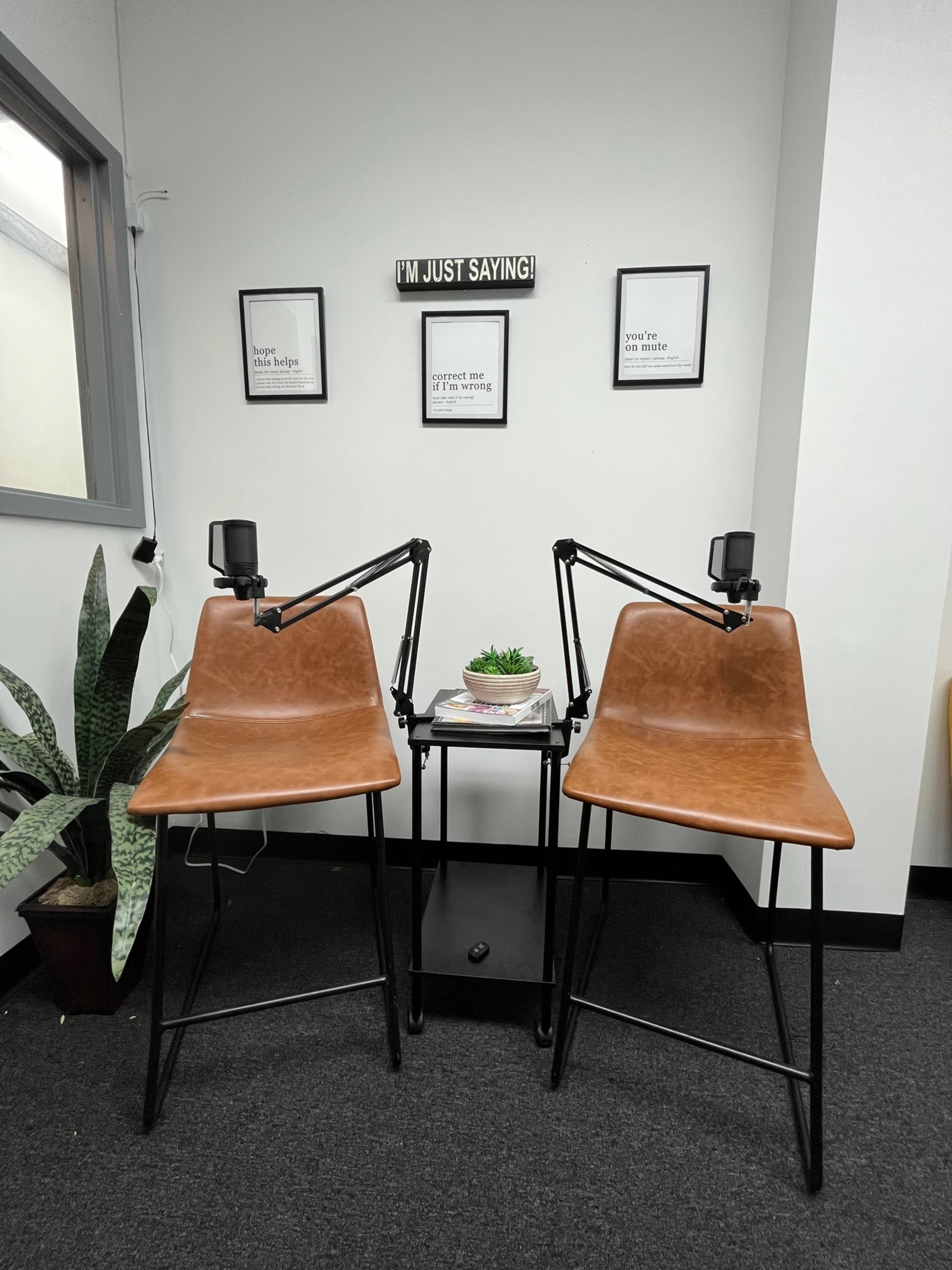 Two chairs are positioned at a small table with a plant in the center, set against a wall with motivational framed quotes.