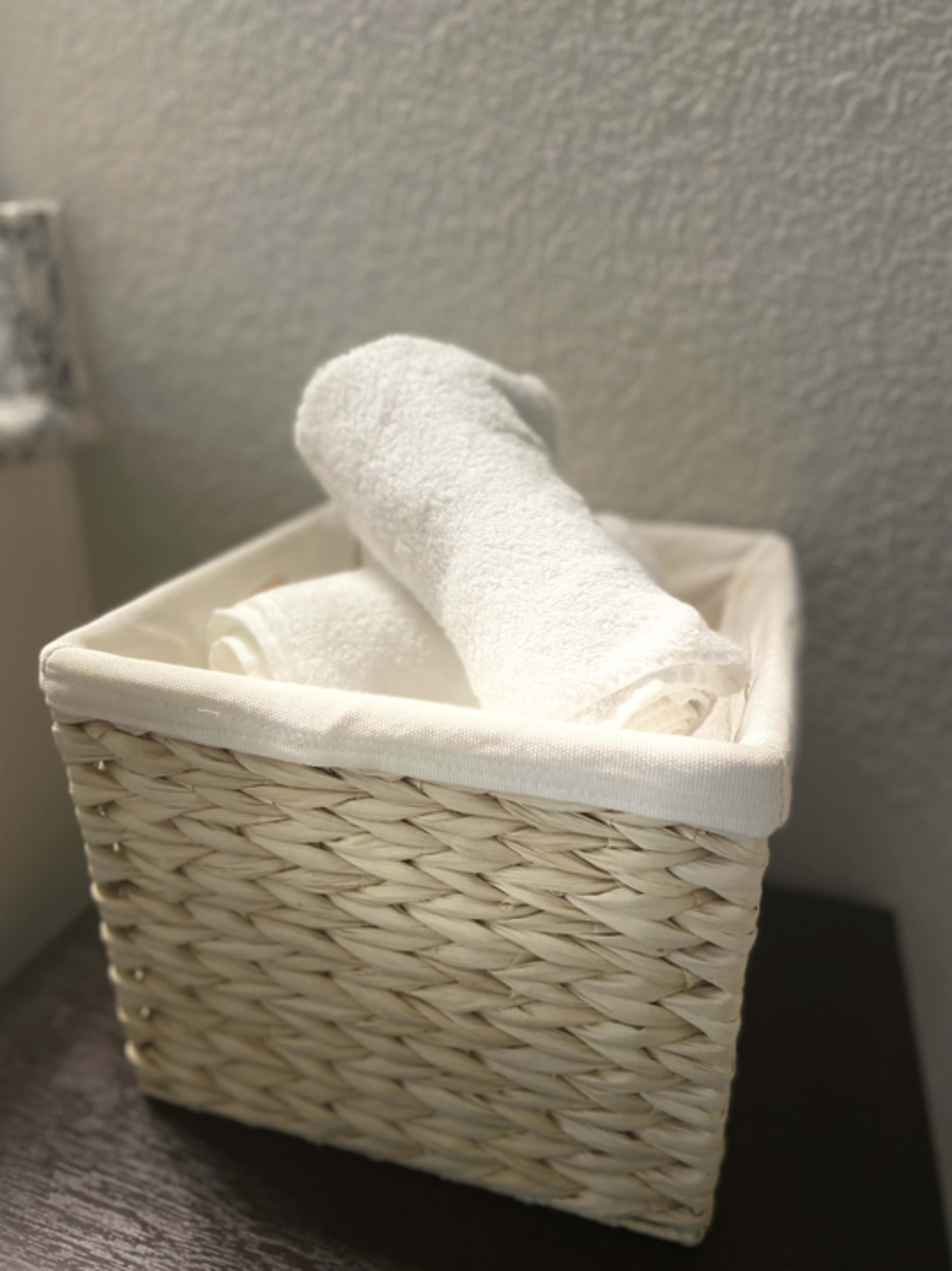 A woven basket containing two rolled white towels sits on a dark surface against a light wall.