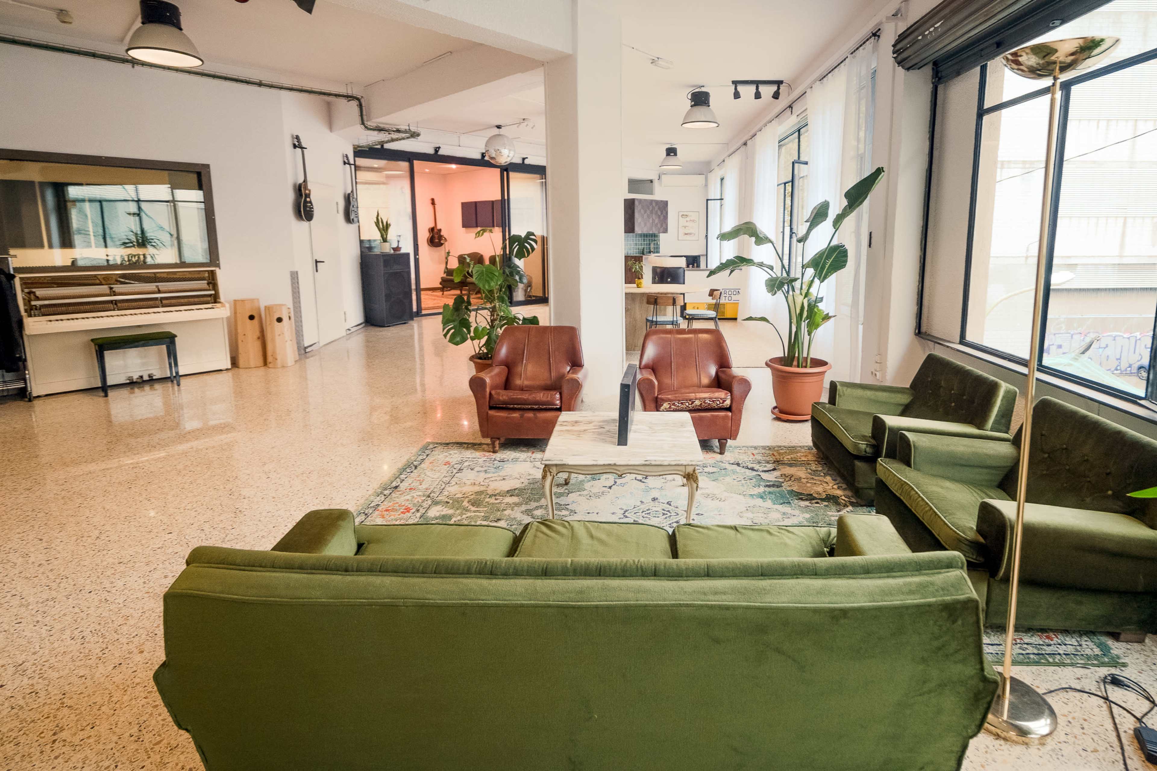 A spacious living area with green couches, a marble coffee table, a piano, and large windows allowing natural light.