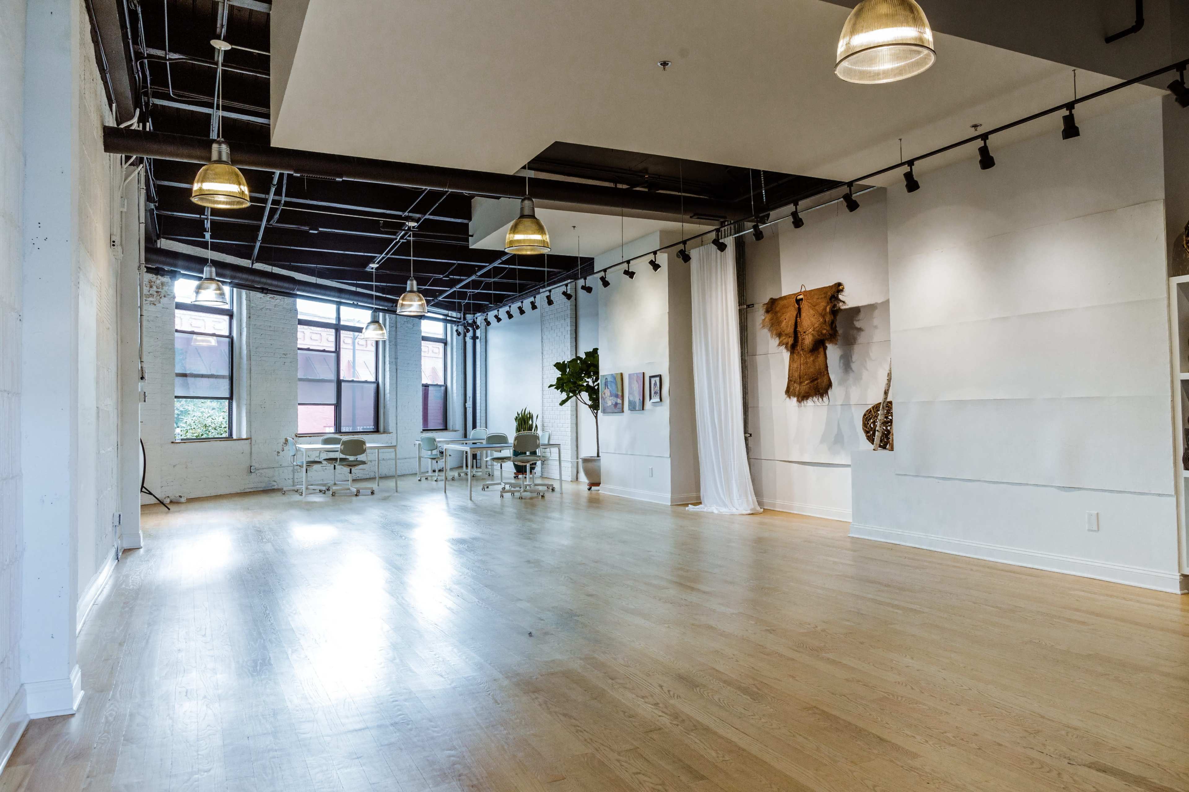 A spacious, well-lit interior with hardwood floors, featuring modern lighting fixtures and a few pieces of artwork on the walls.